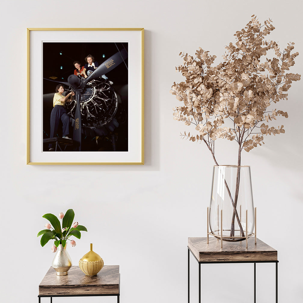 A print of vintage photography featuring women working on an airplane, framed and hung with other decor