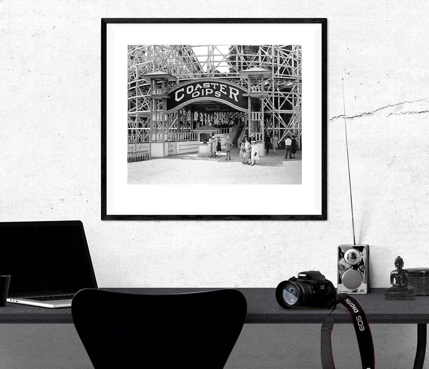 A framed paper print hanging above a desk, featuring vintage photography of Coaster Dips rollercoaster