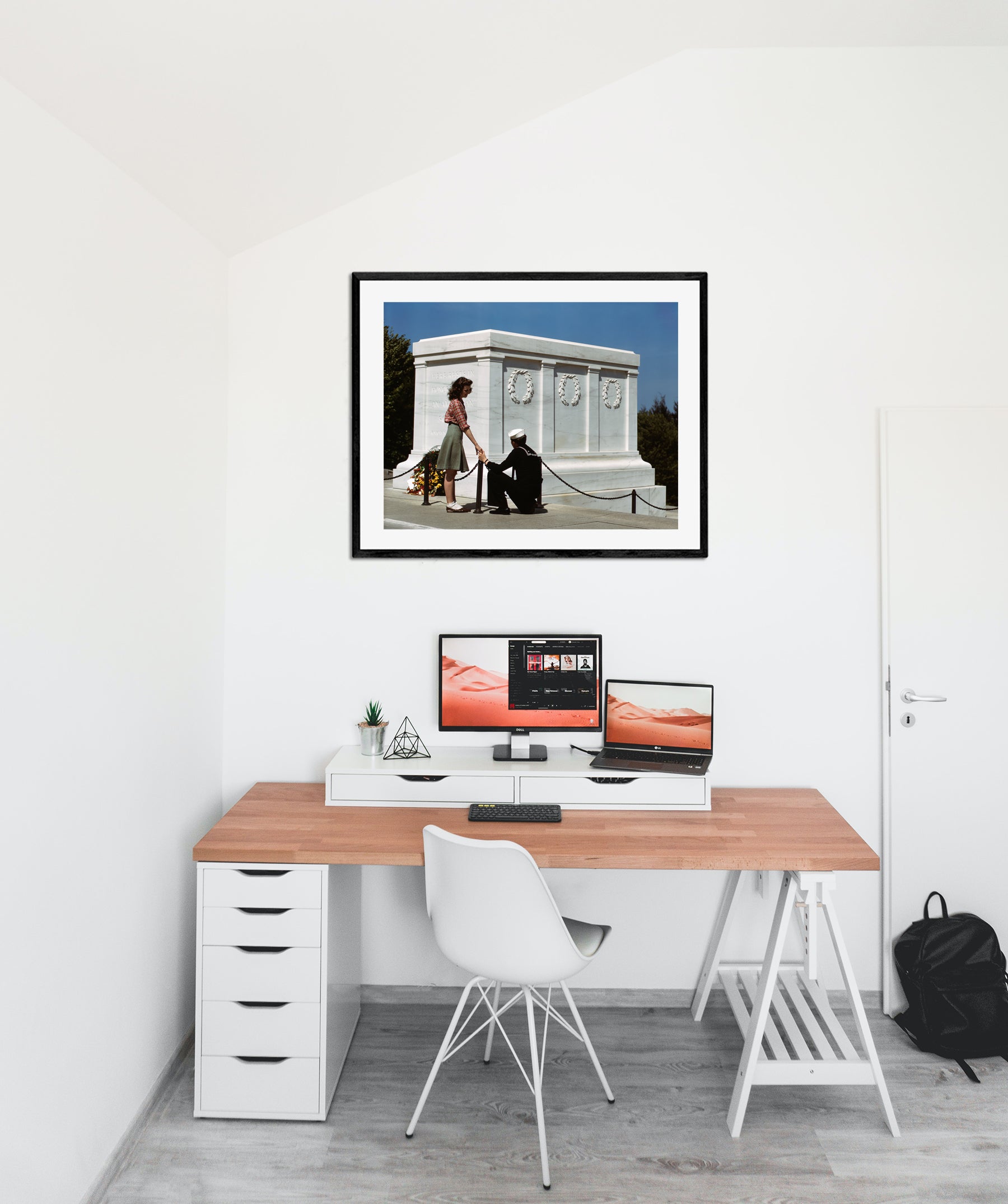 A stark office space with a framed paper print hanging on the wall above the desk