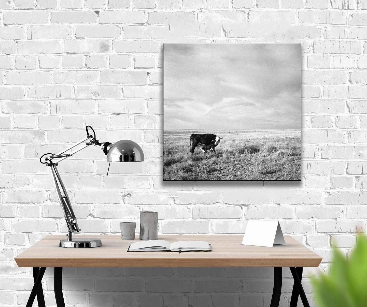 A desk in front of a white brick wall with a canvas printing of a vintage photograph hanging on it