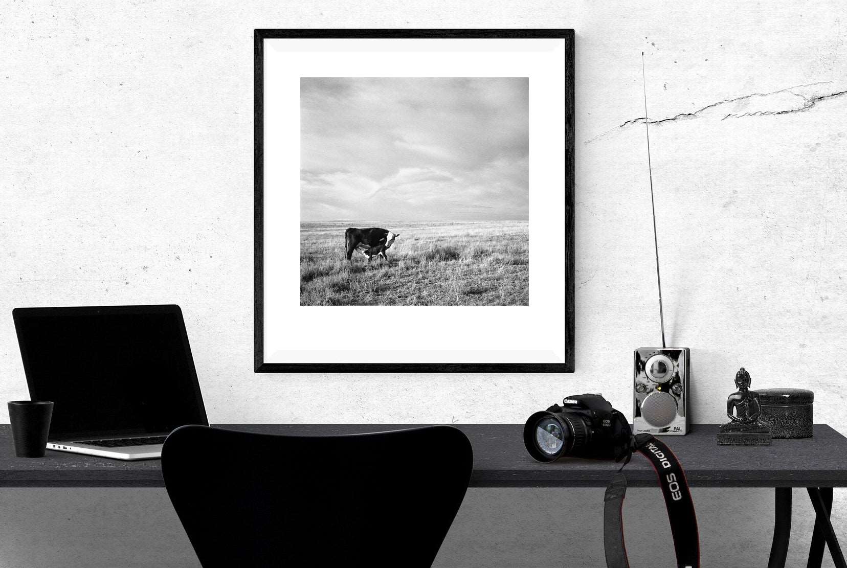 A workspace with a framed paper print on the wall, featuring a vintage photograph of grazing cows in Oregon