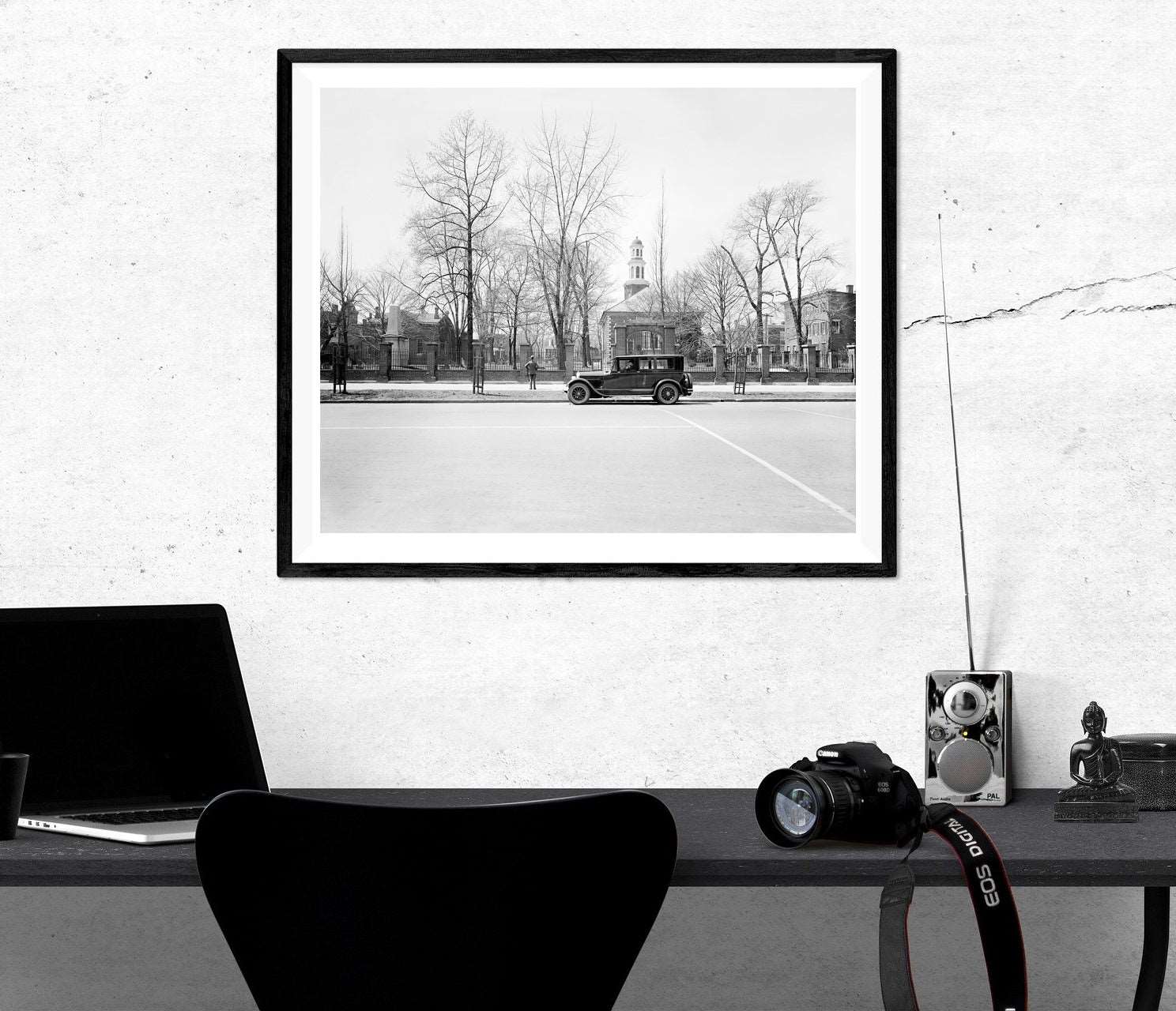 A photo of a desk with a framed paper print on the wall, featuring vintage photography in Alexandria
