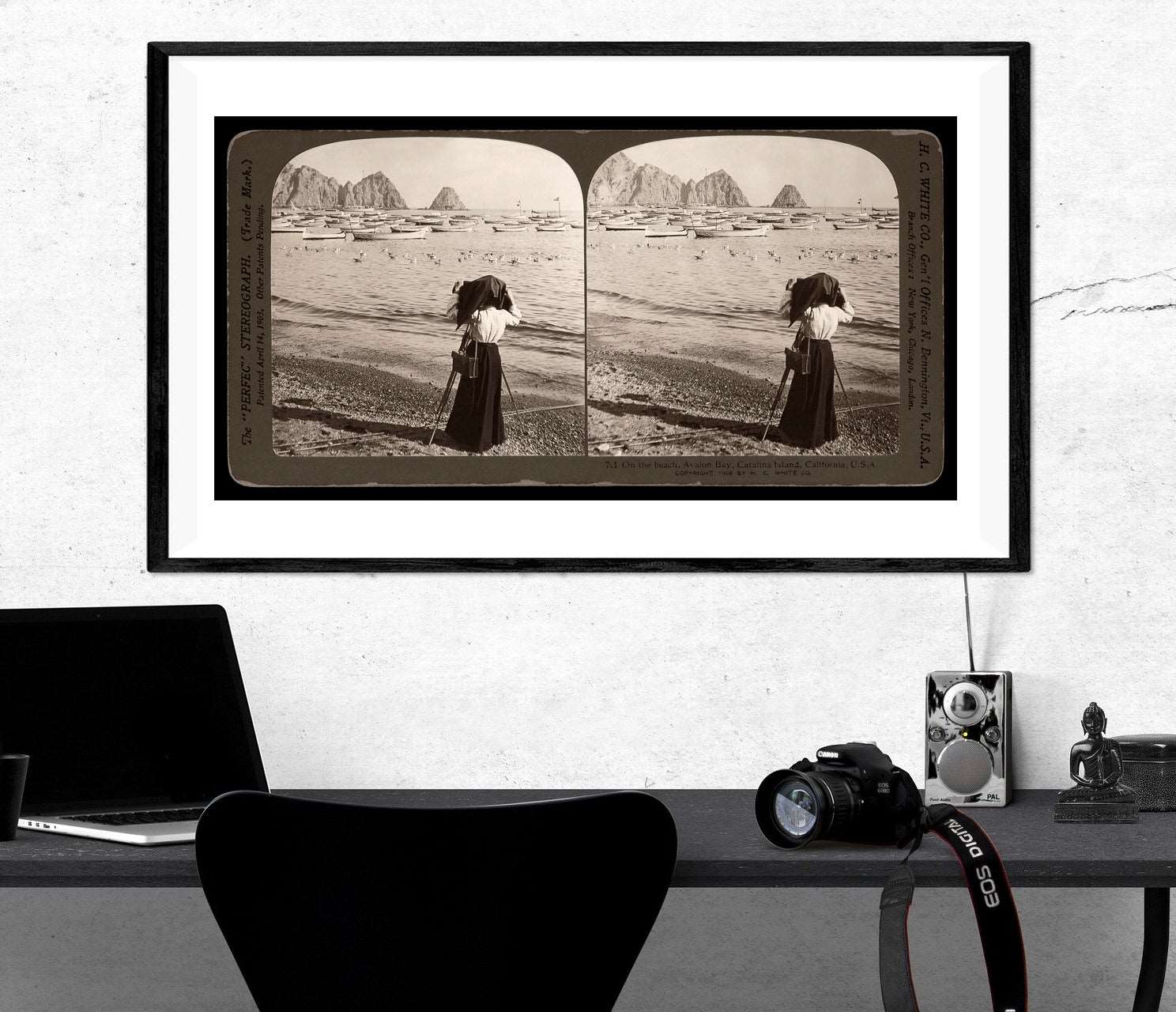 A desk with a framed paper print of a vintage stereograph photo hanging on the wall above