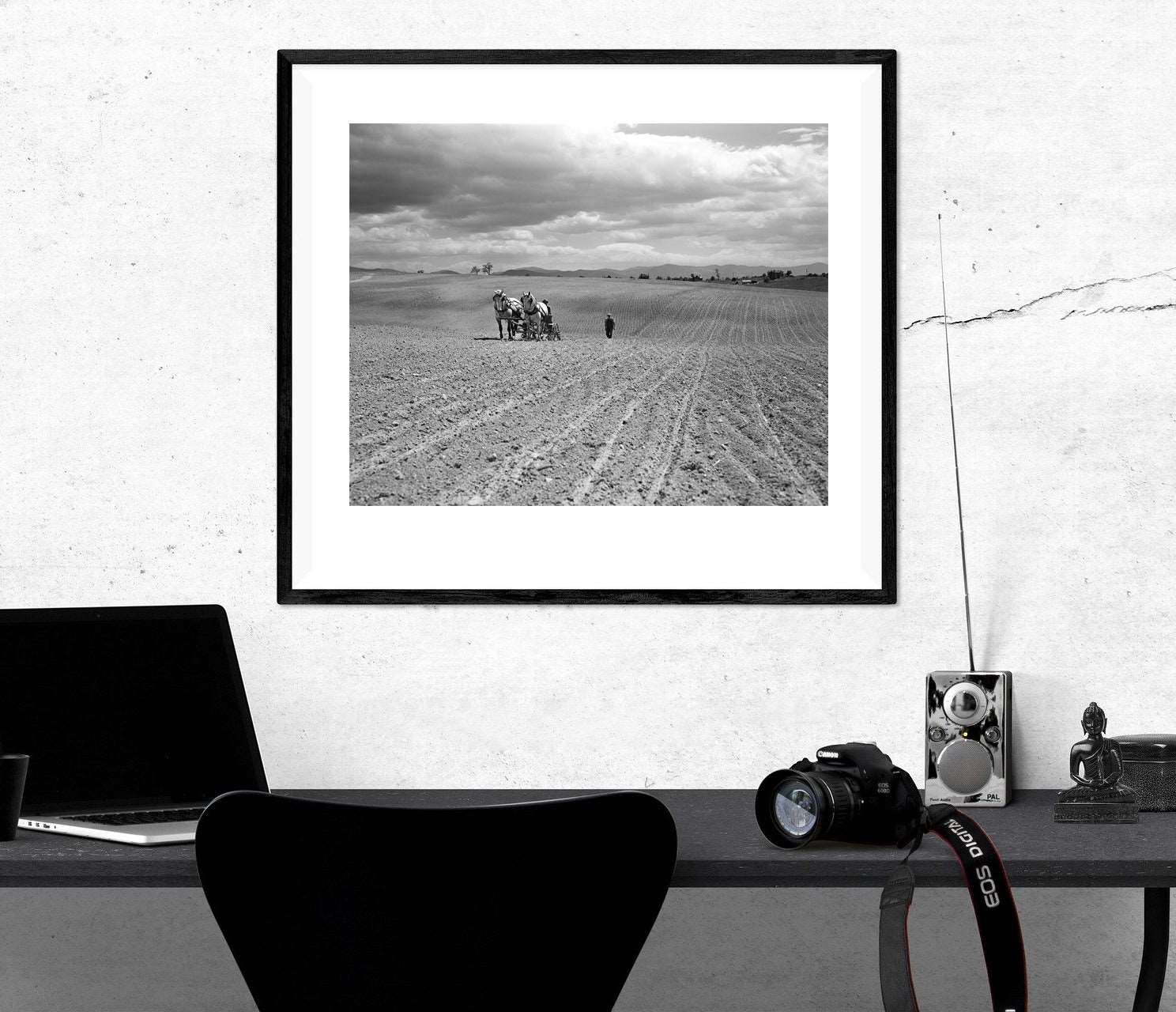 A framed paper print of a vintage photograph hanging on a white wall above a desk