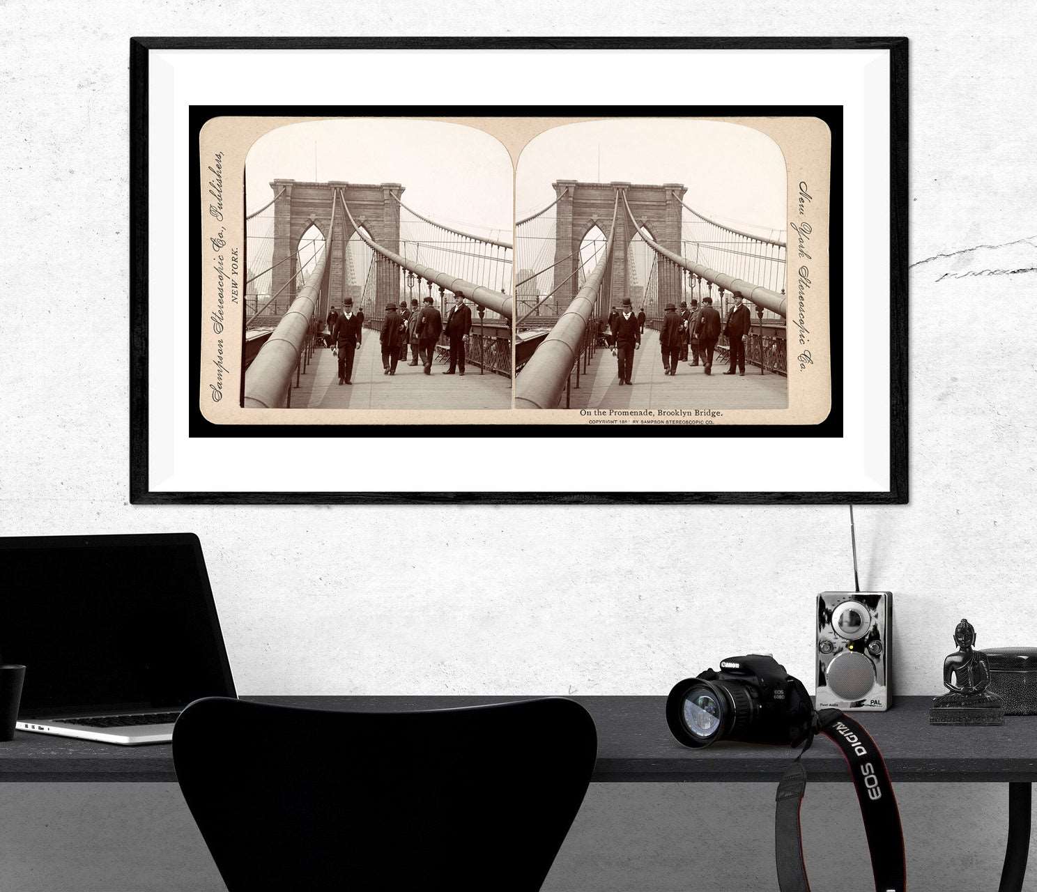 A framed paper print of a vintage stereograph image hanging on a wall above a black desk