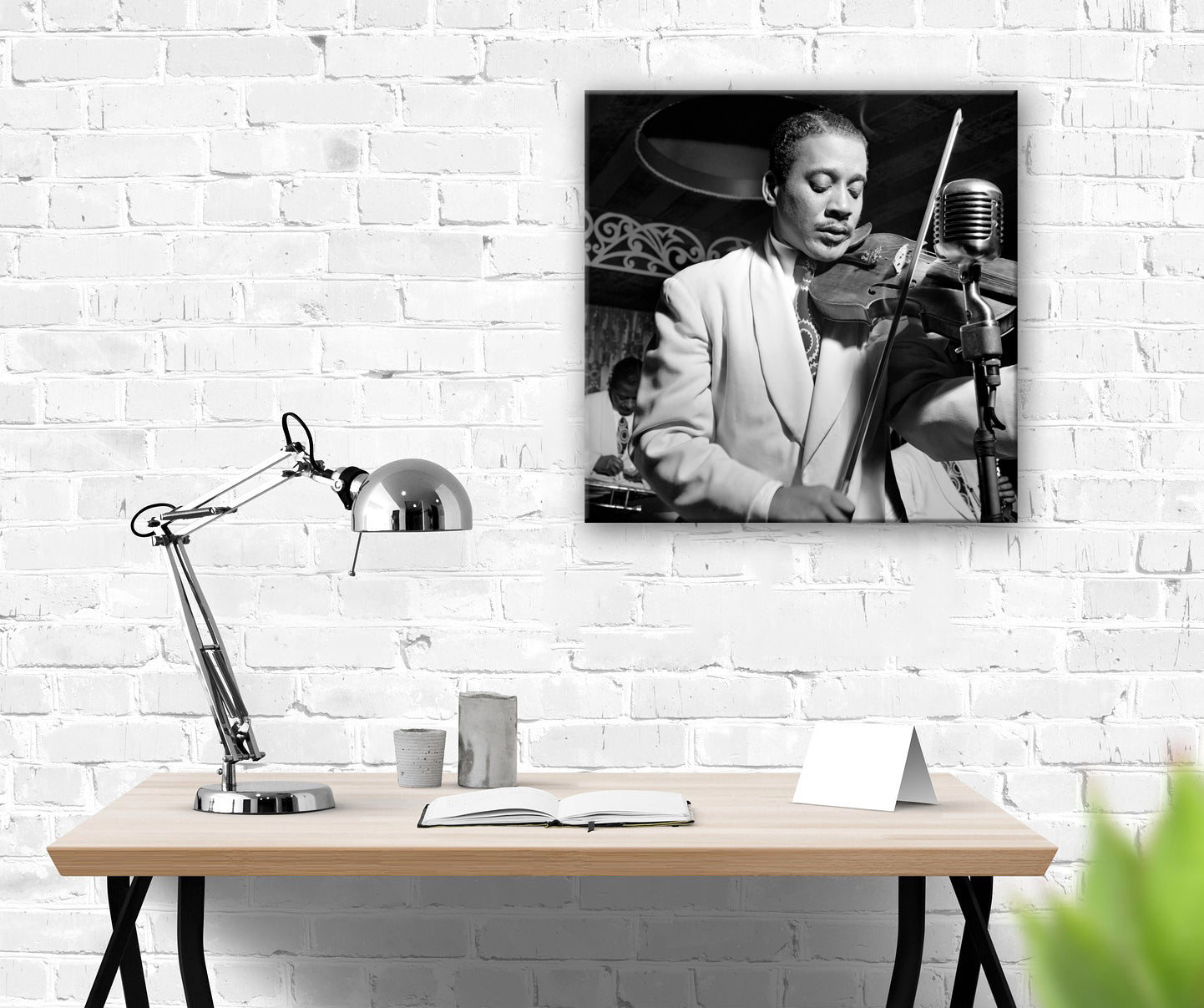 A desk in front of a white brick wall, with a stretched canvas print of a photograph of Ray Nance