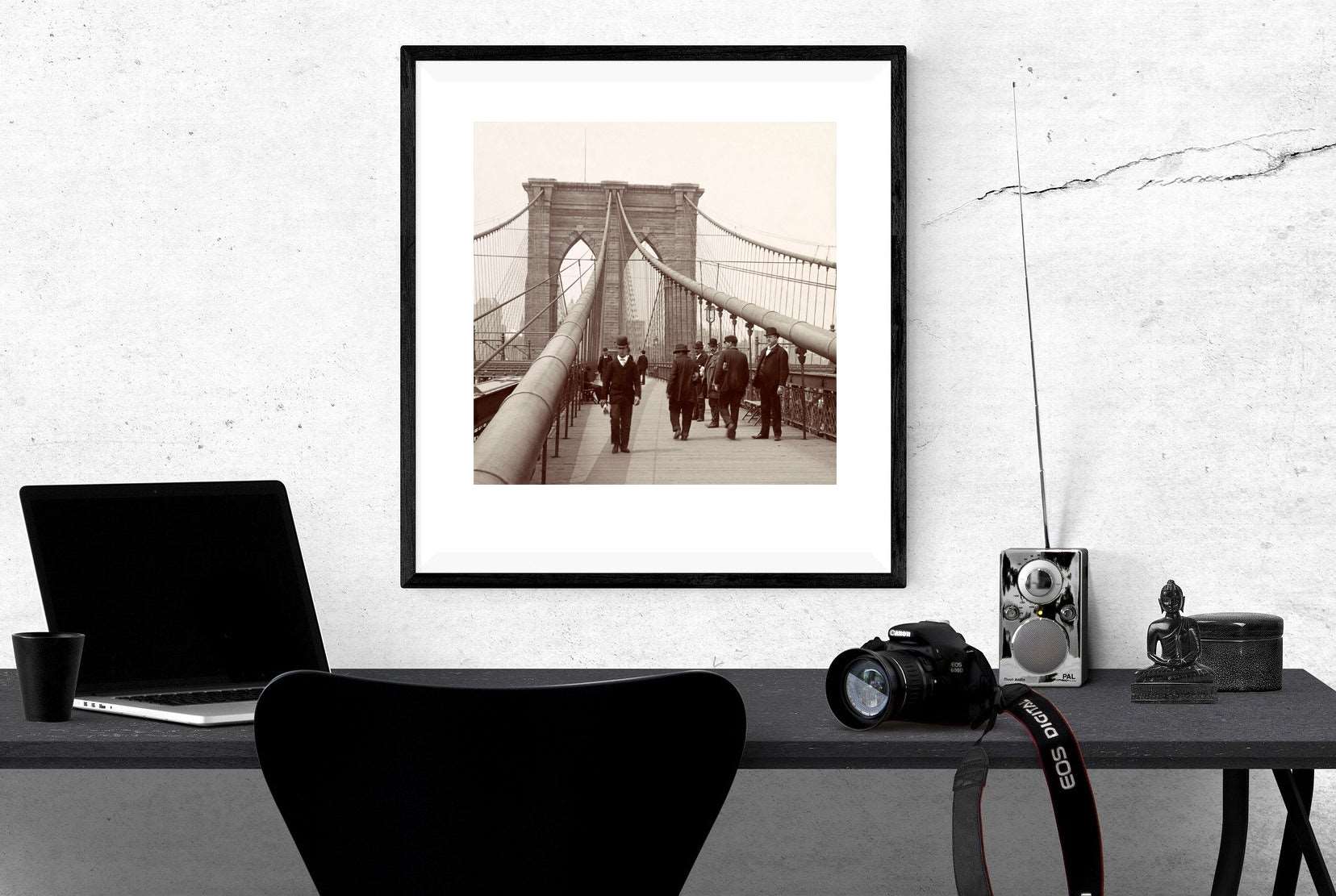 A framed vintage photograph of people walking on the Brooklyn Bridge hanging above a desk