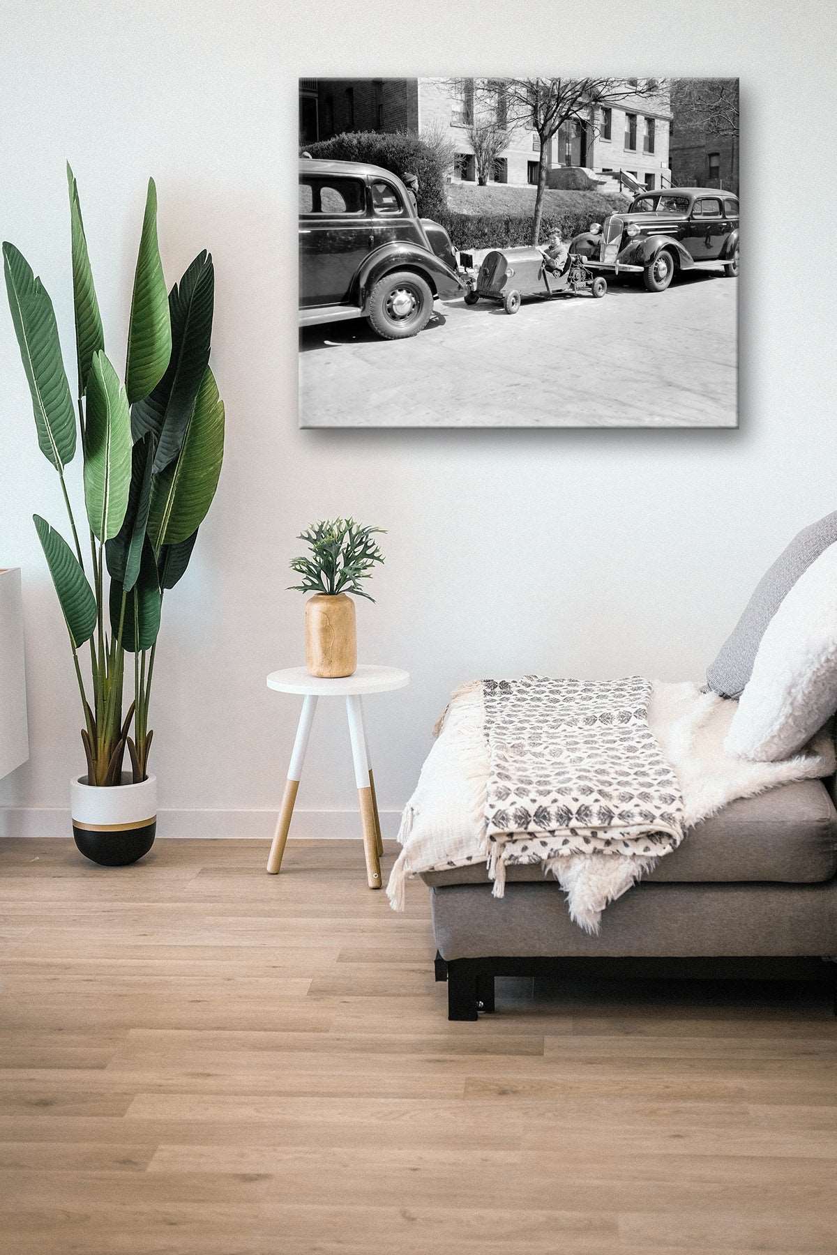 A canvas print reproduction hanging in a living room, featuring a vintage photograph of a boy parking his miniature car