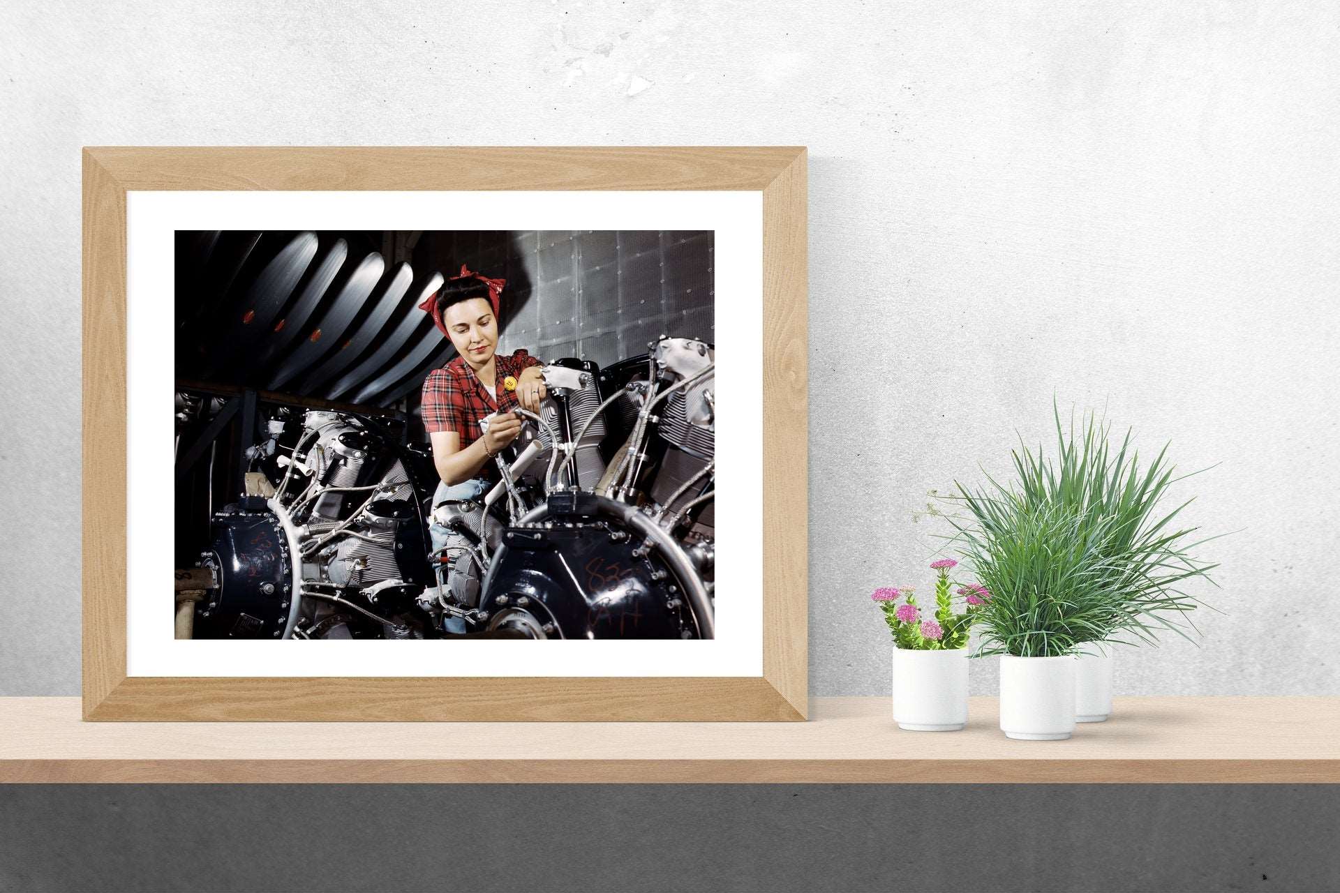 A small framed print of a vintage photograph of a woman working on a plane, sitting next to plants on a table