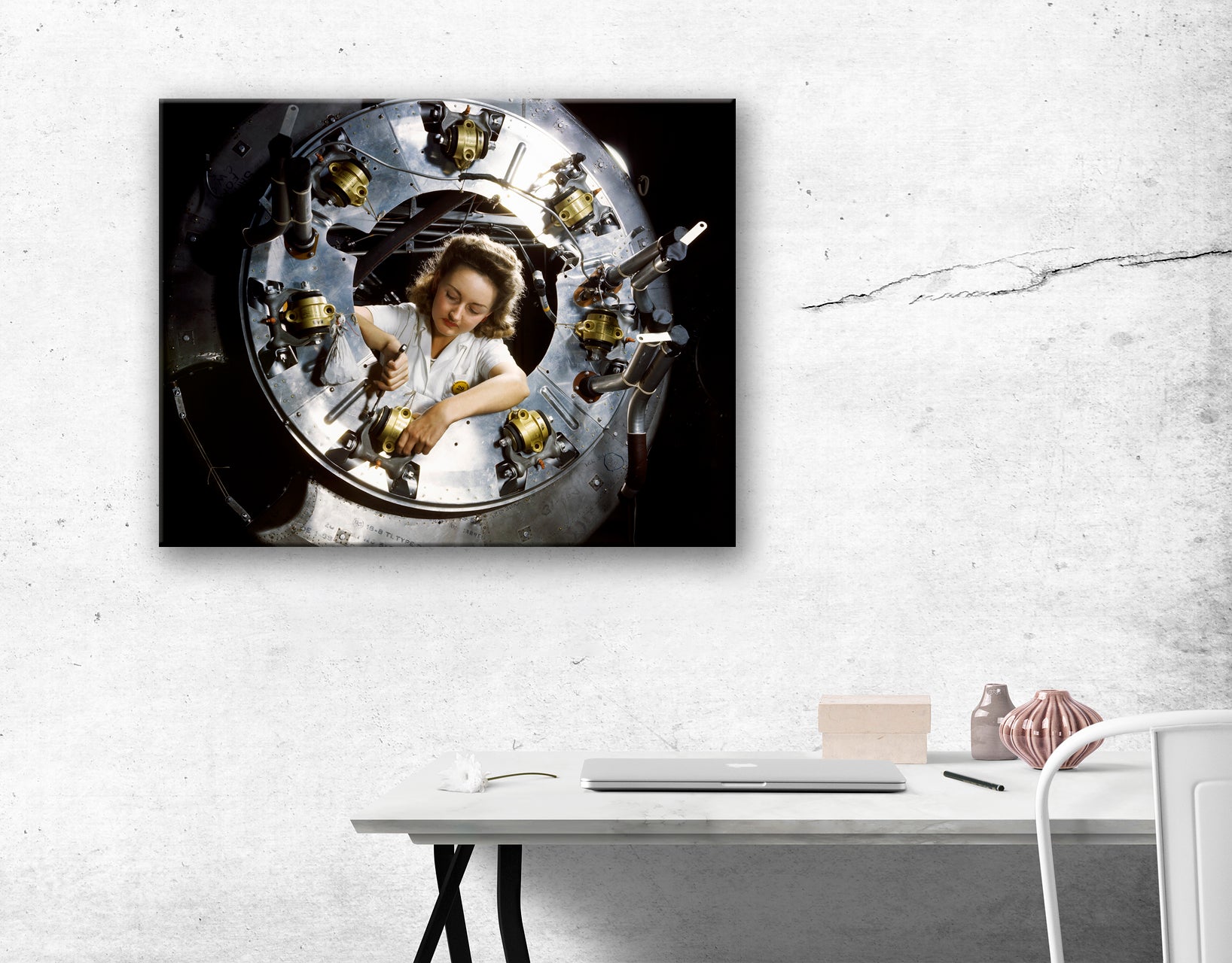 A rendering of a canvas print hanging above a desk, featuring a photograph of a woman working on a motor part of a B-25 bomber