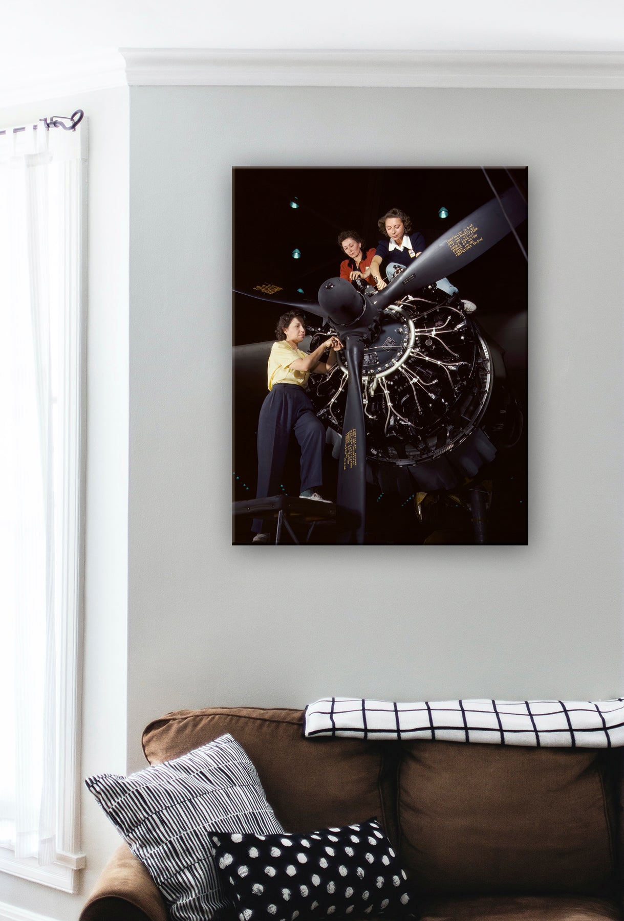 A digital rendering of a canvas reproduction of a photograph of women working on a plane, displayed above a couch
