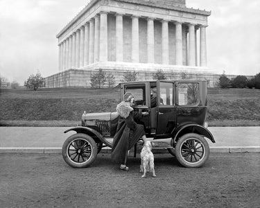 A vintage image of a woman standing outside a Ford vehicle in front of the Lincoln Memorial