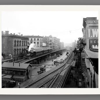 Vintage black and white photograph of a New York City street with train tracks, buildings, and people, printed on paper.