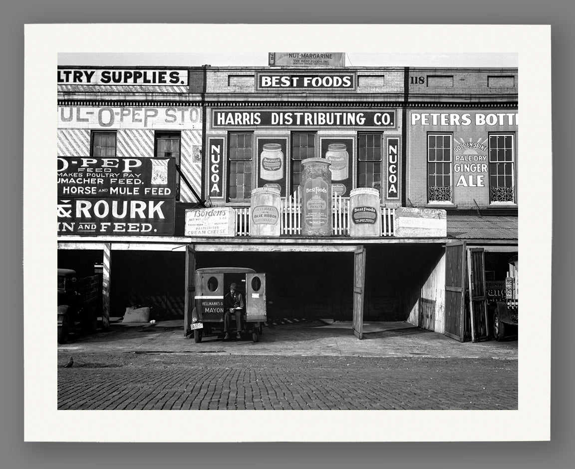A fine art paper print of a vintage image of warehouses along the waterfront in Louisiana, featuring many advertisements