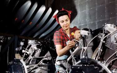 A vintage, color photograph of a woman working on an airplane motor