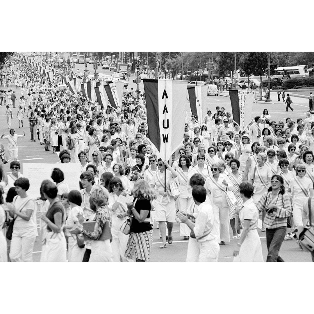 Black and white photograph of a large group of people marching with signs, including one with 'AAUW'.