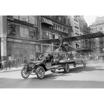 A vintage photograph of a plane being pulled by a car in a 4th of July Parade in New York City