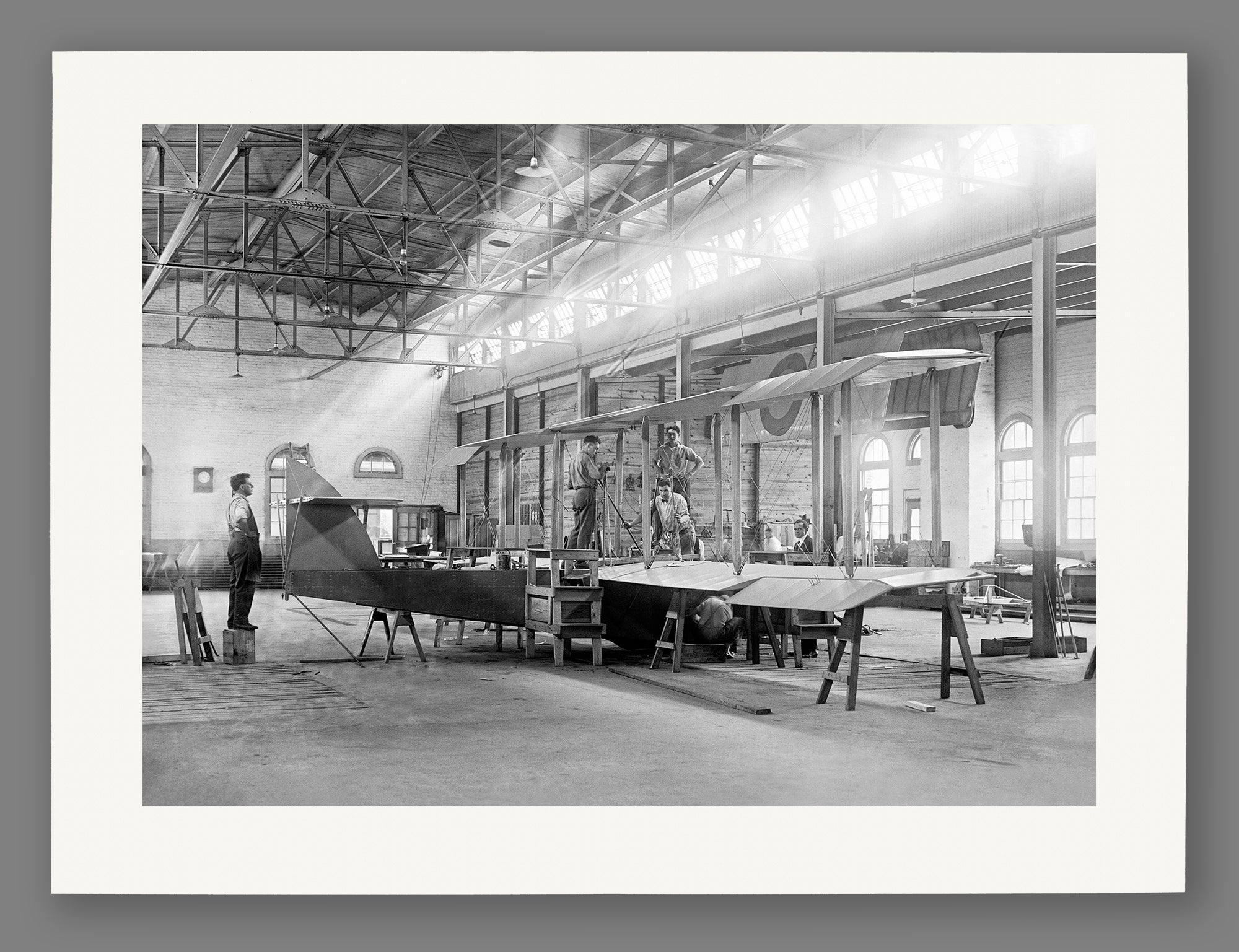 A paper reproduction print of a black and white photograph of an airplane factory