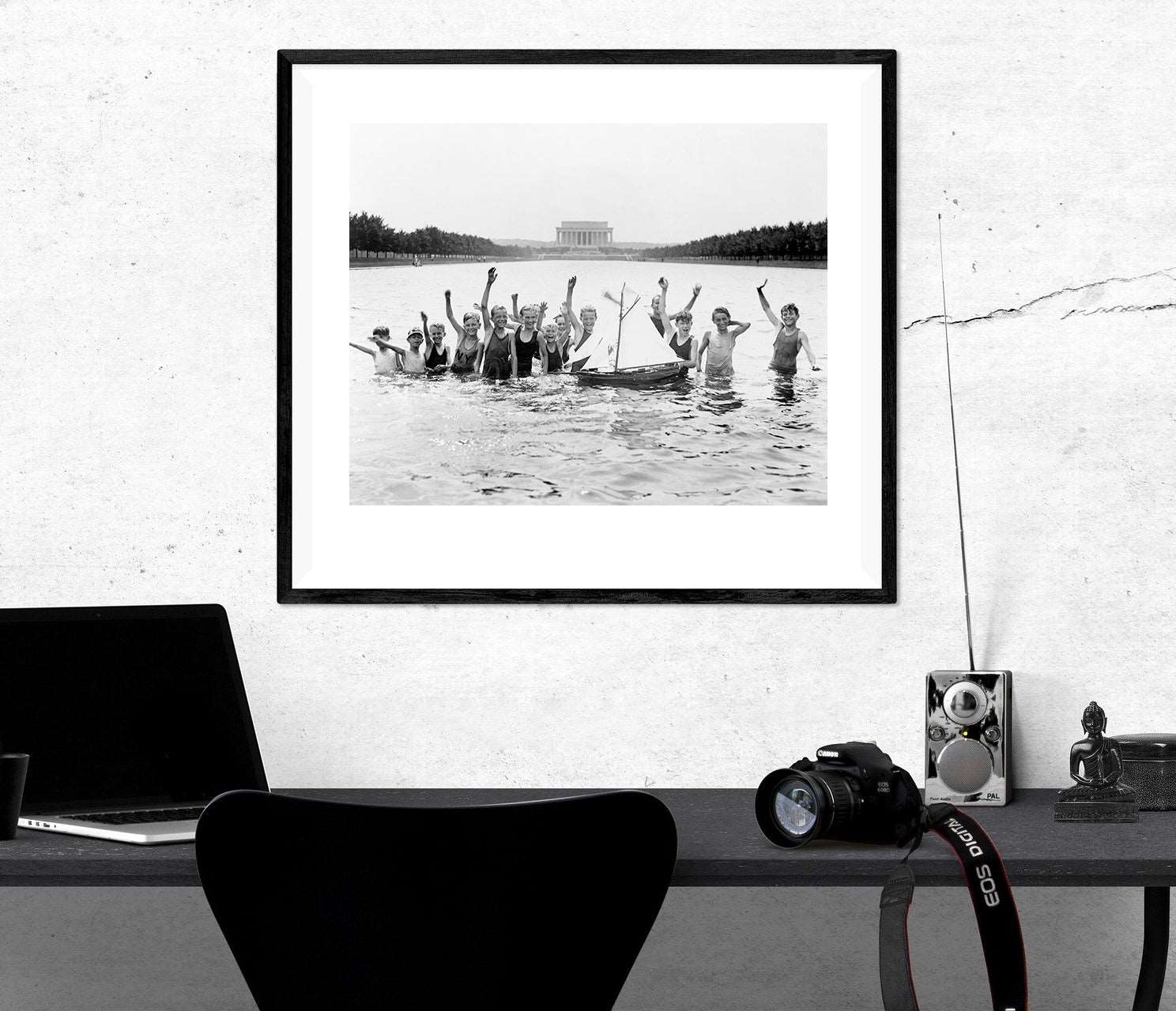 A framed print of a photograph of boys in the Reflecting Pool hanging above a black desk