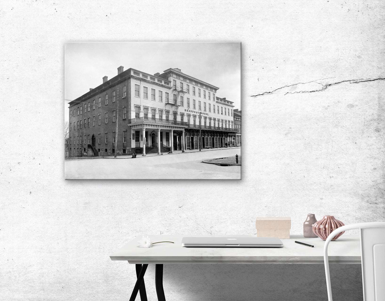 A canvas print of a vintage photograph of the Braddock House hanging on a white wall above a desk