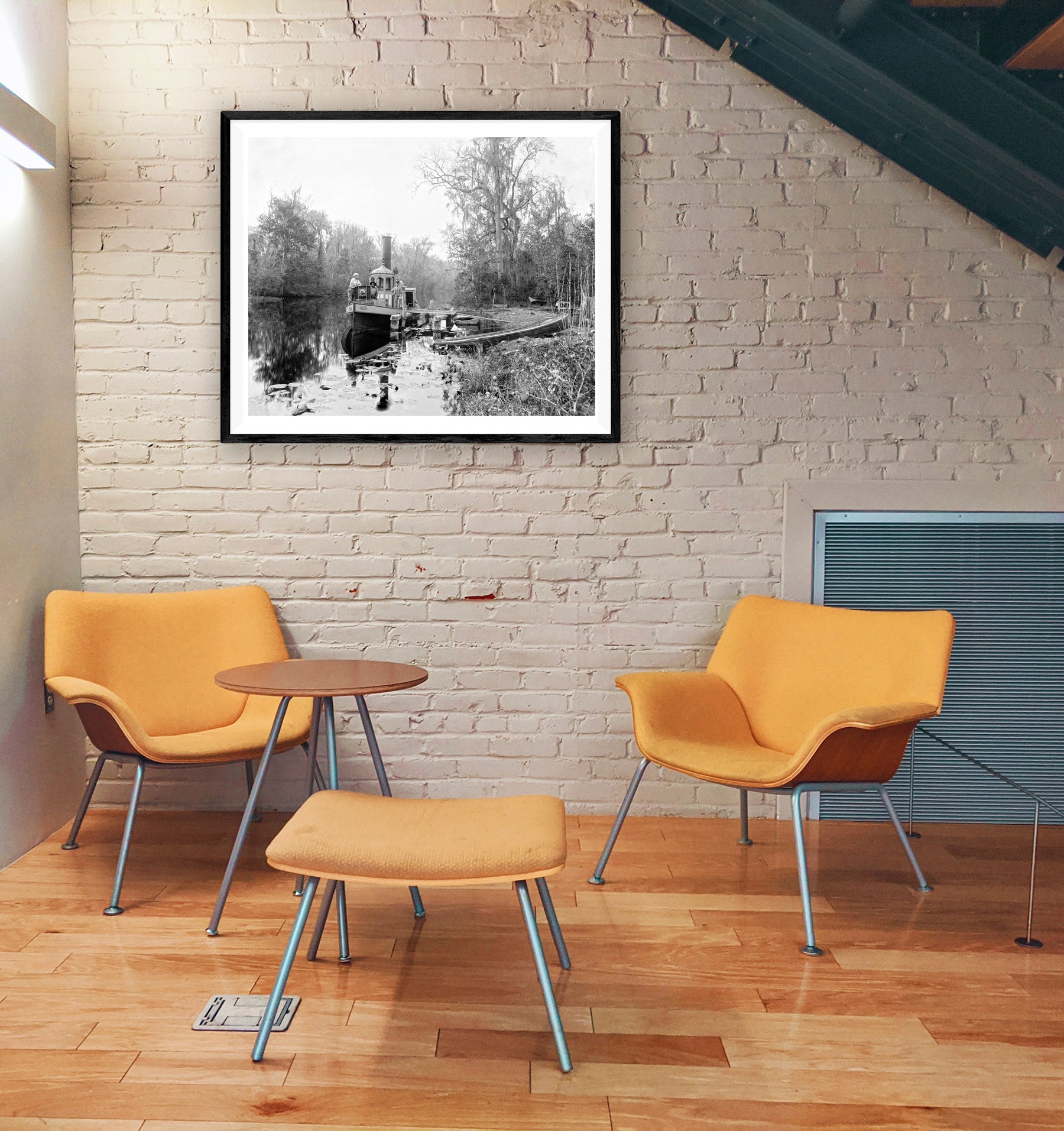 A framed print of a vintage image of Rice Creek hanging on a brick wall in a workspace