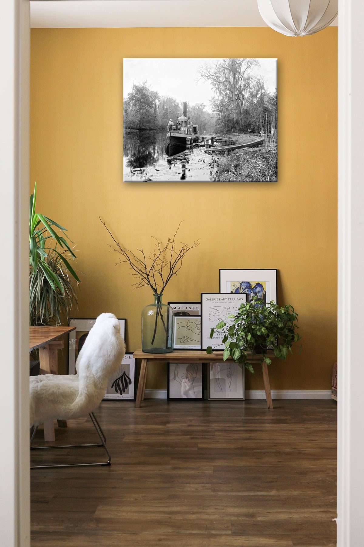 A canvas print of a photograph of Browns Landing hanging on a yellow wall above a collection of frames