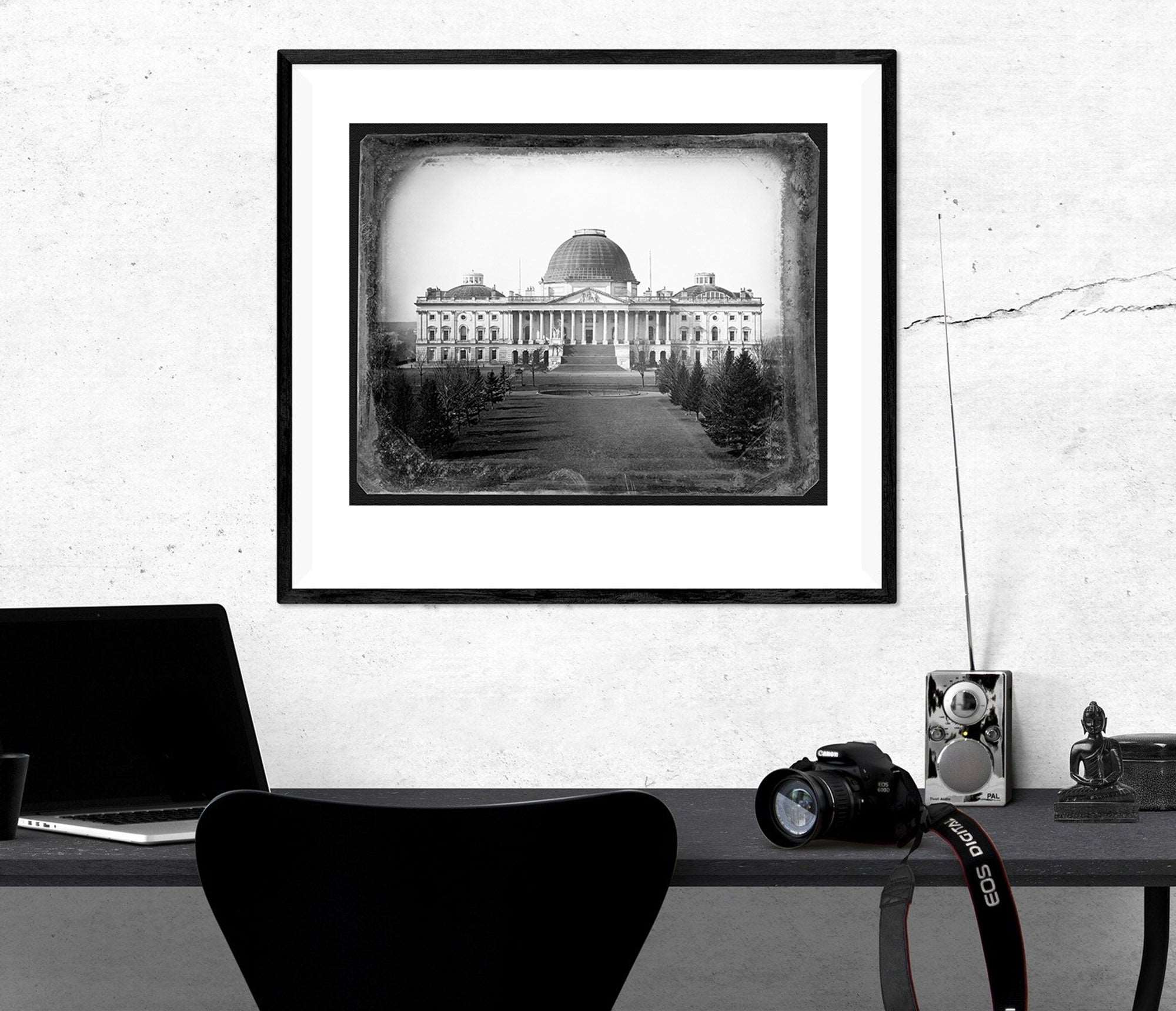 A paper print of a photograph of the Capitol Building, framed and hanging on a wall above a desk