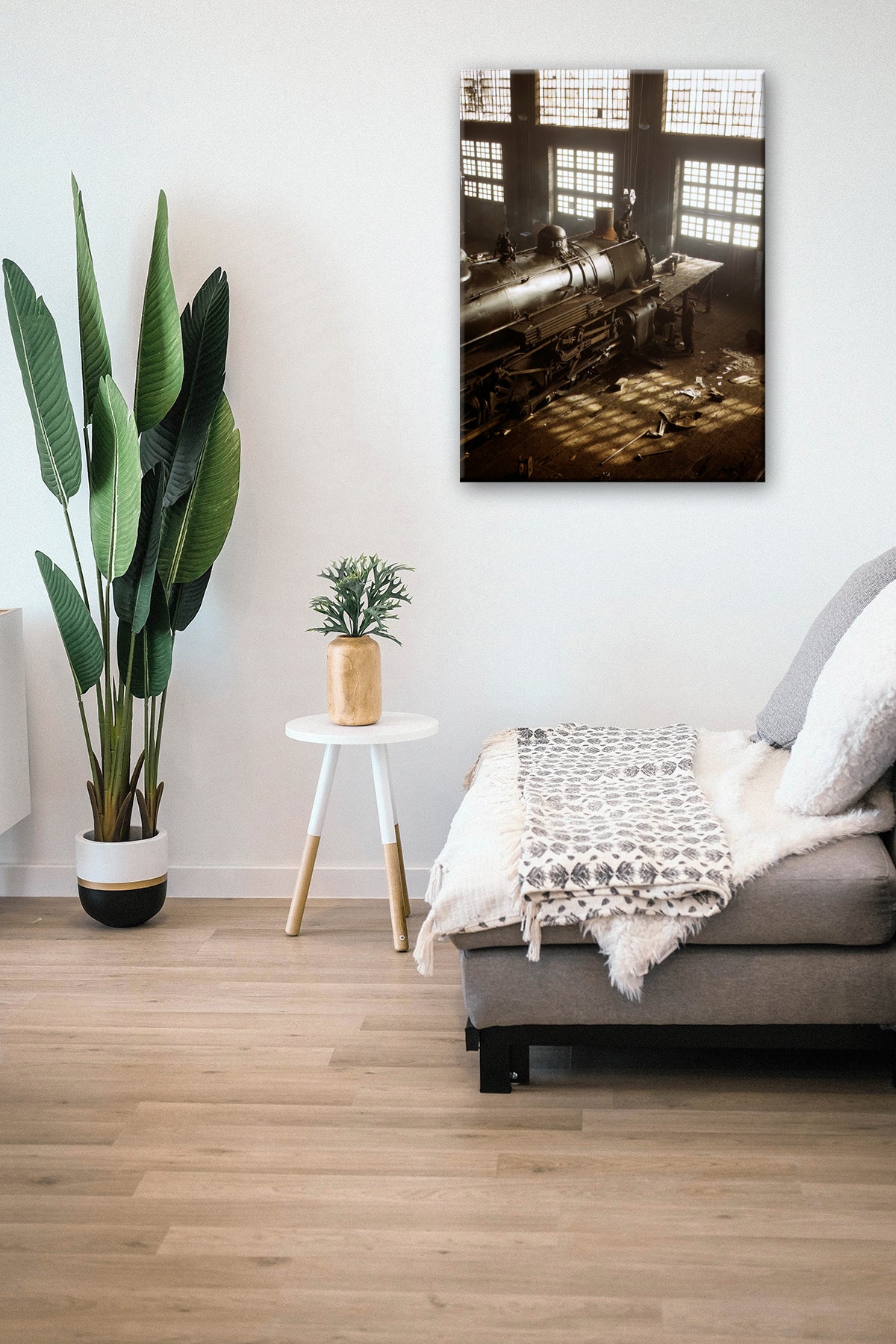 A canvas print of a vintage photograph of Railroad Shops hanging next to a tall plant in a living room