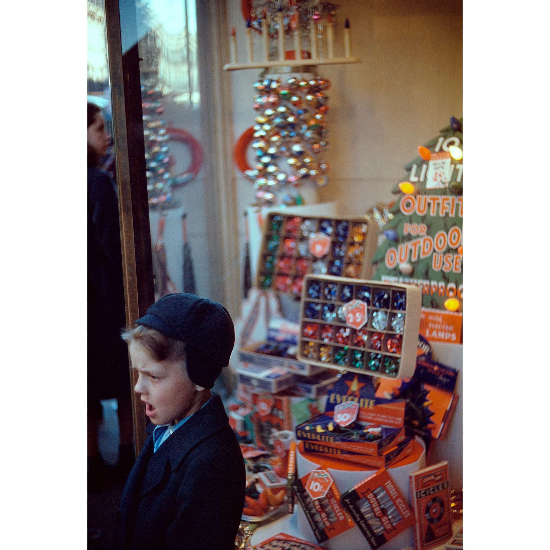 A vintage color photograph of a boy in front of a Christmas display in the window of a store