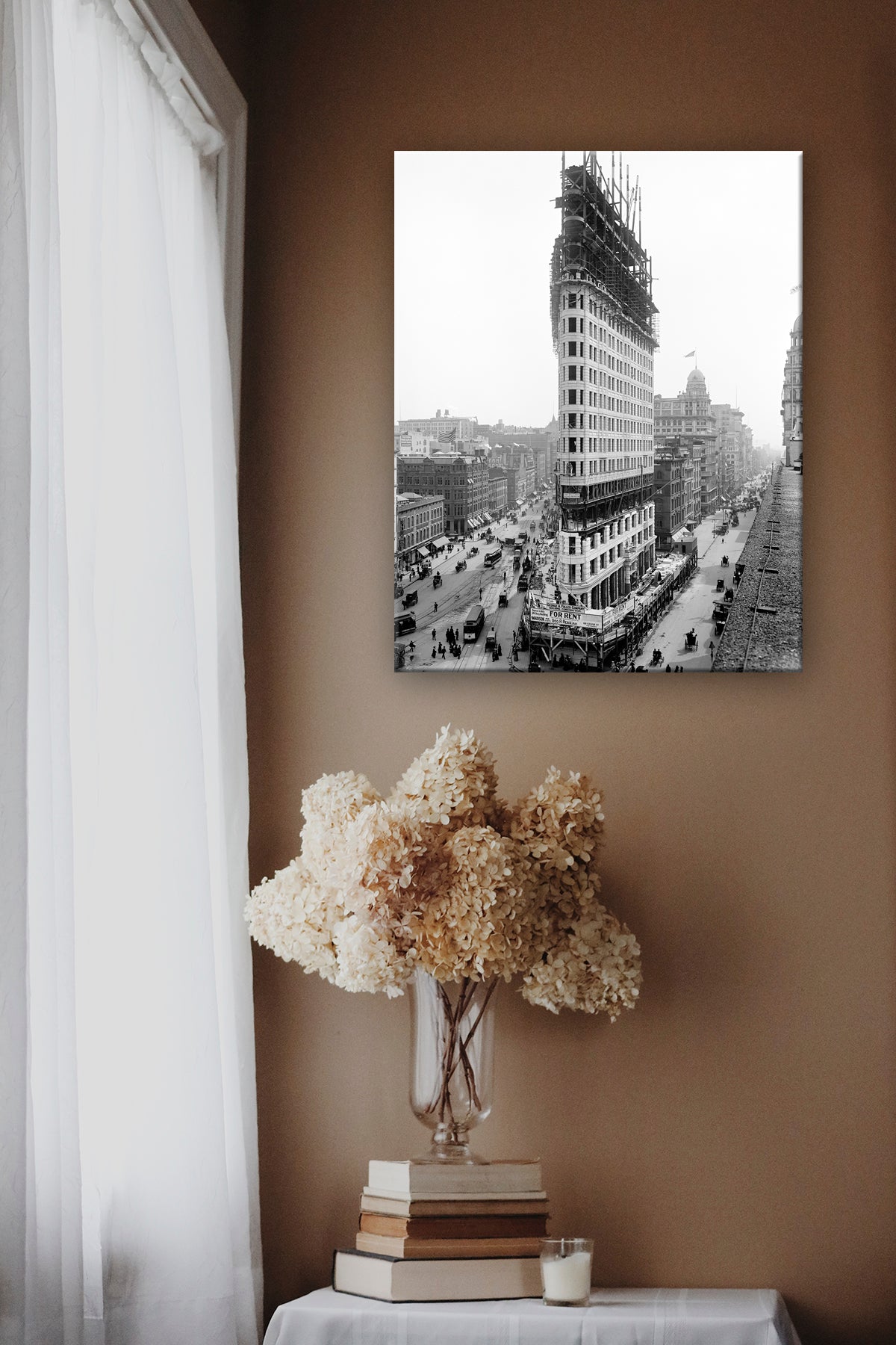 A canvas print of vintage photography depicting New York City hanging on a brown wall above a vase of flowers