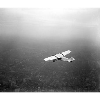 A vintage black and white photograph of a Ford Motor Company Plane in flight above a city