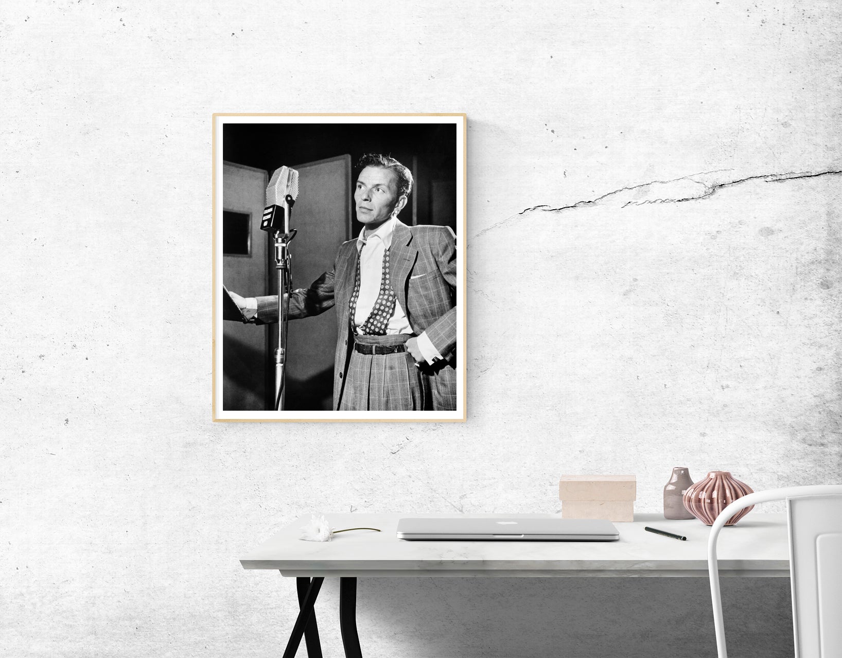 A mockup of a framed paper print of Frank Sinatra, hanging on a white wall above a desk