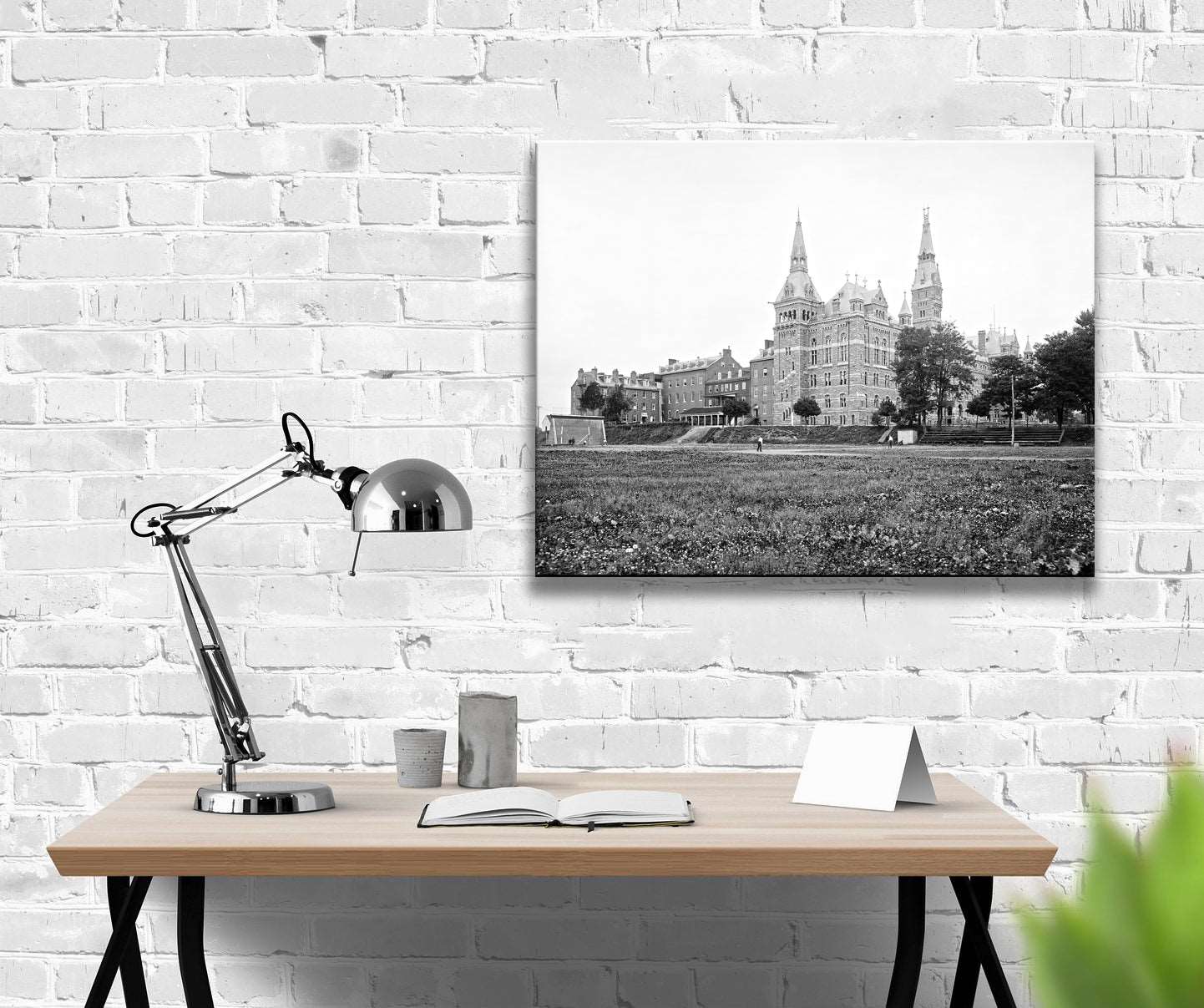 A canvas print of a vintage photograph of Georgetown University hanging on a brick wall above a desk