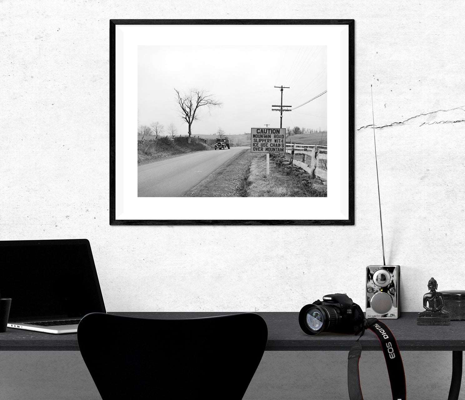A framed paper print on the wall above a desk, featuring vintage photography of a car on the highway