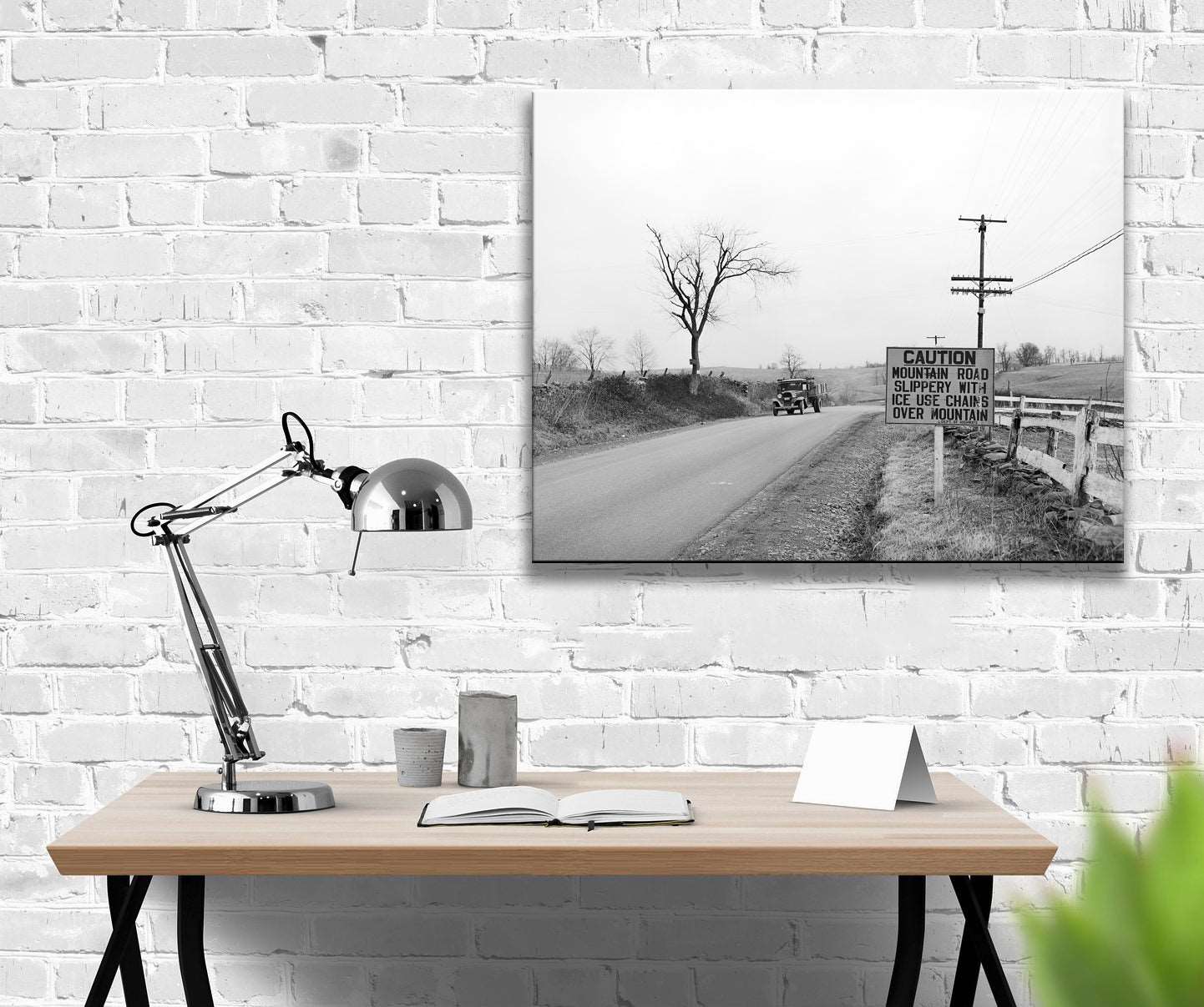 A photo of a canvas print hanging above a desk, featuring a vintage photograph of a car on the highway