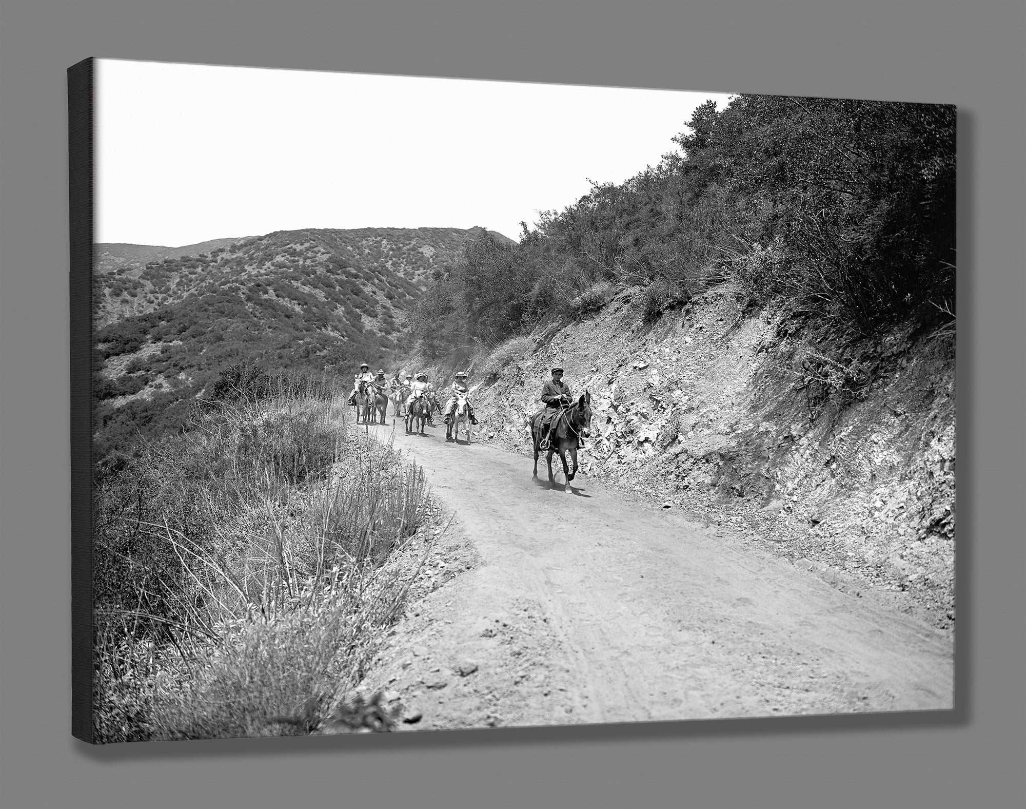 A canvas reproduction print of a vintage photograph of people on horseback on a trail