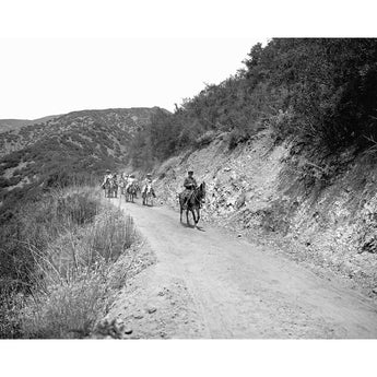 A vintage photograph of a group of people riding horses on a trail through hills