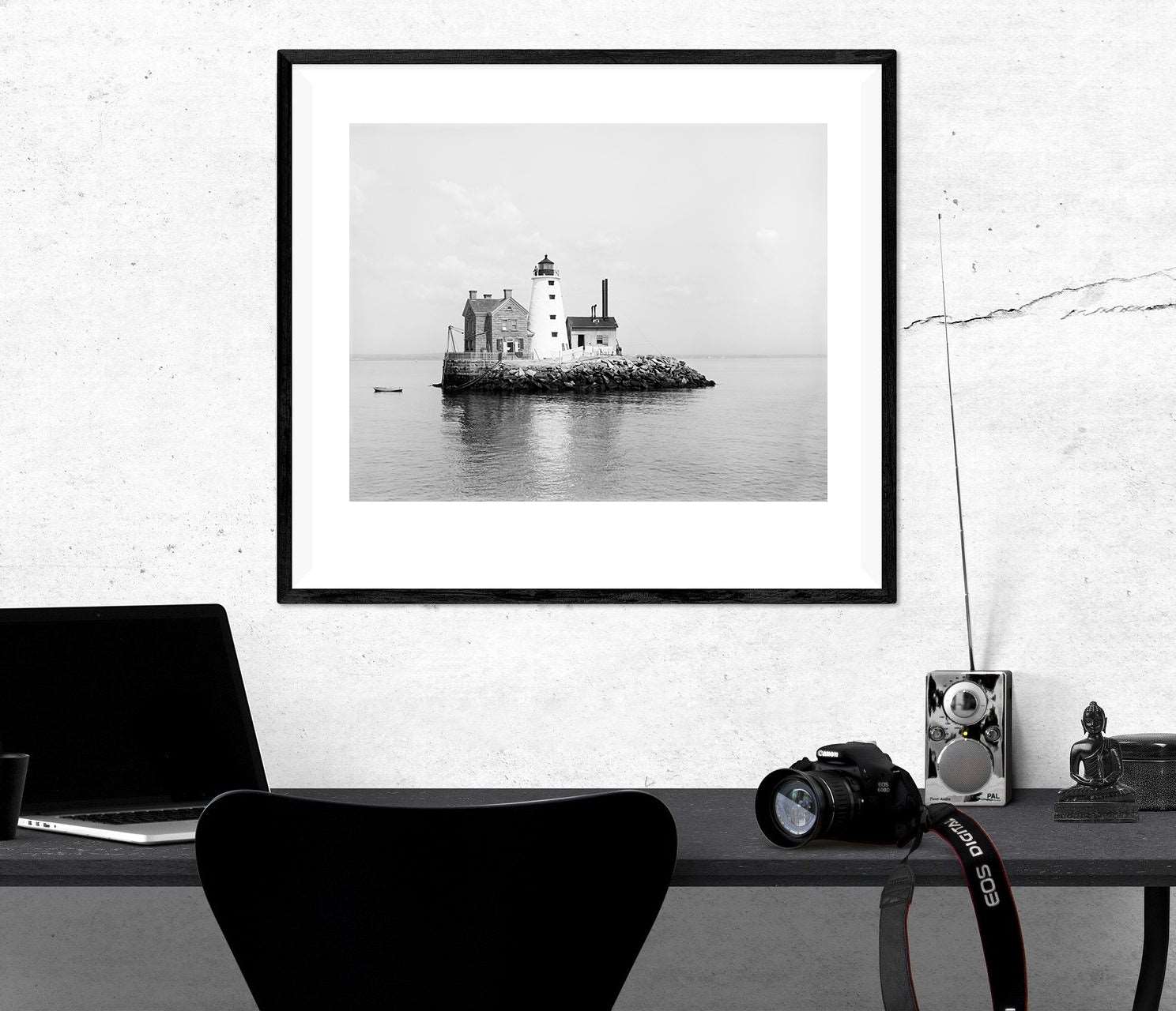 A framed paper print of a vintage photograph of a lighthouse, hanging on a white wall