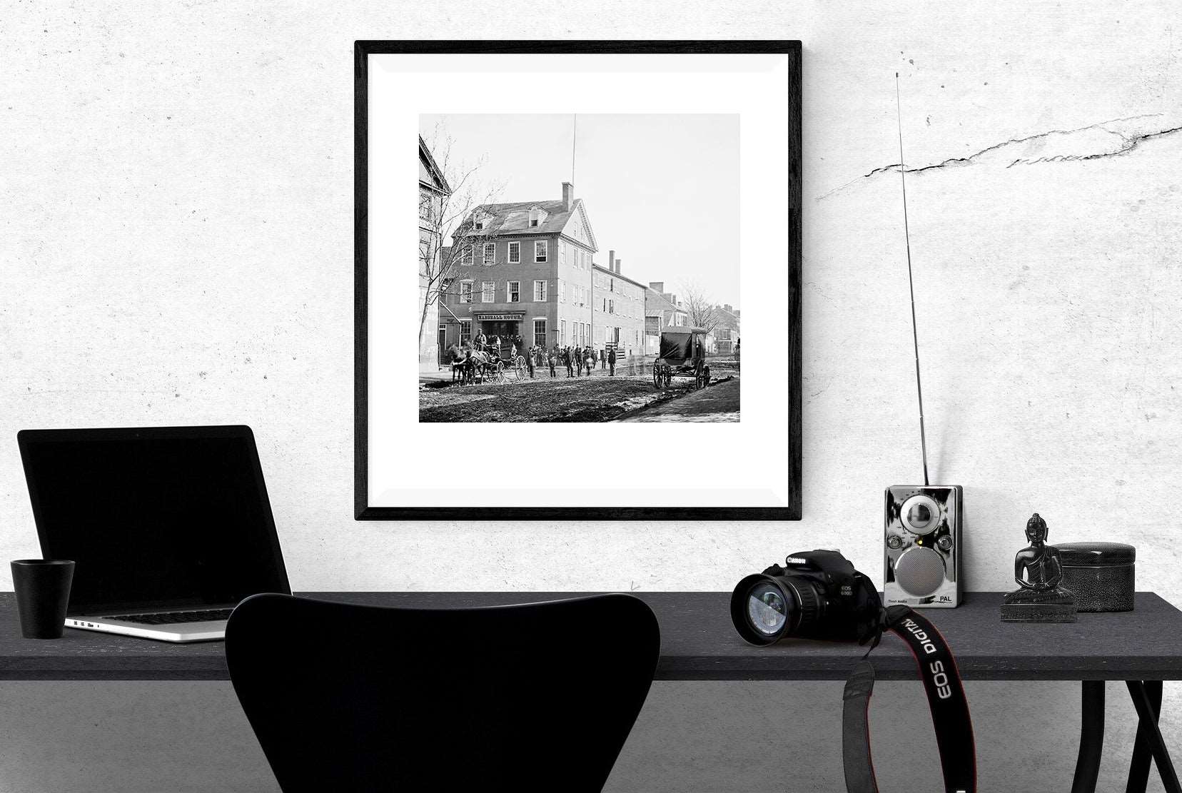 A framed paper print of a photograph of the Marshall House in Alexandria hanging above a work desk