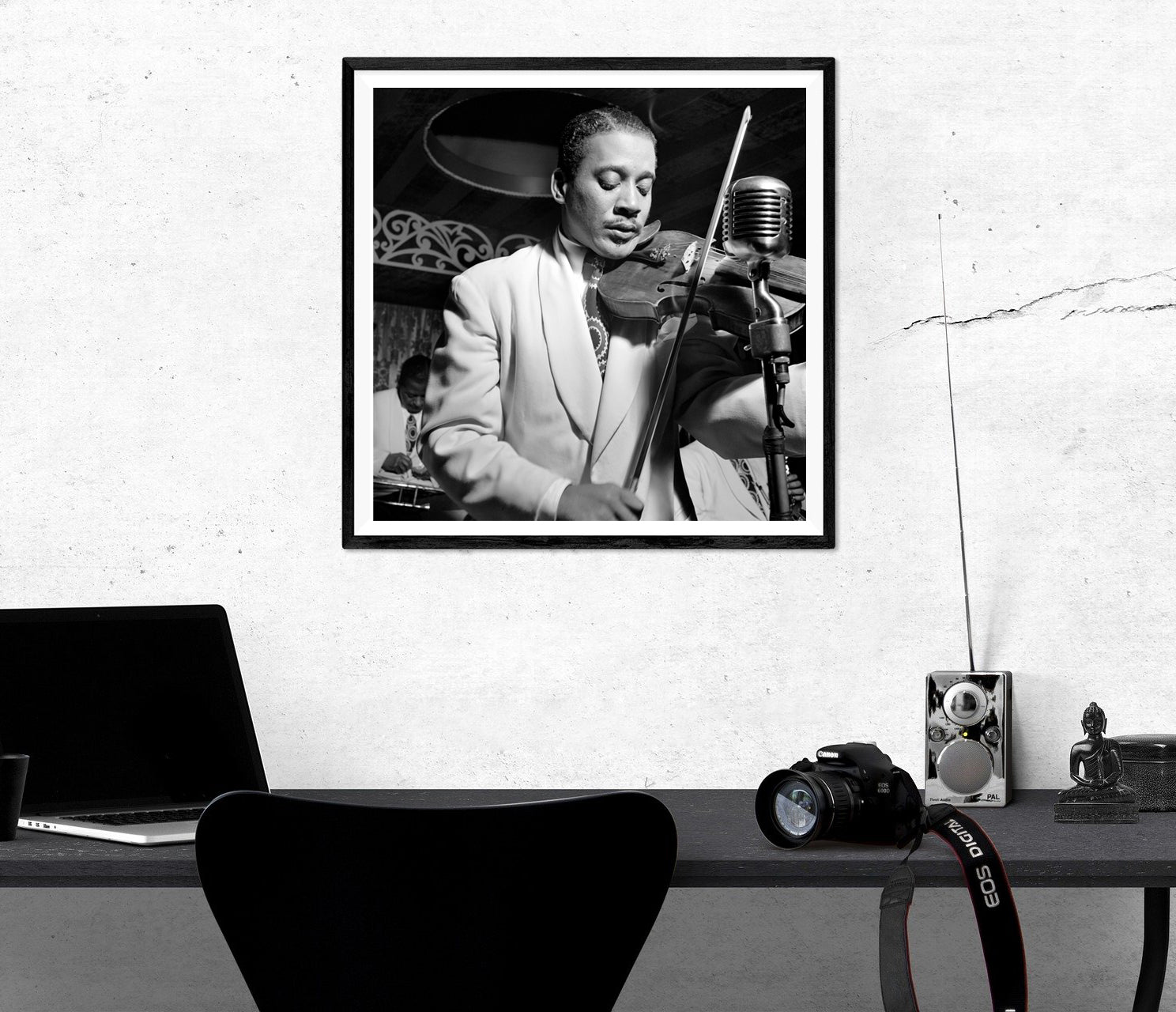 A framed reproduction print of a photograph of Ray Nance hangs on a wall above a black desk