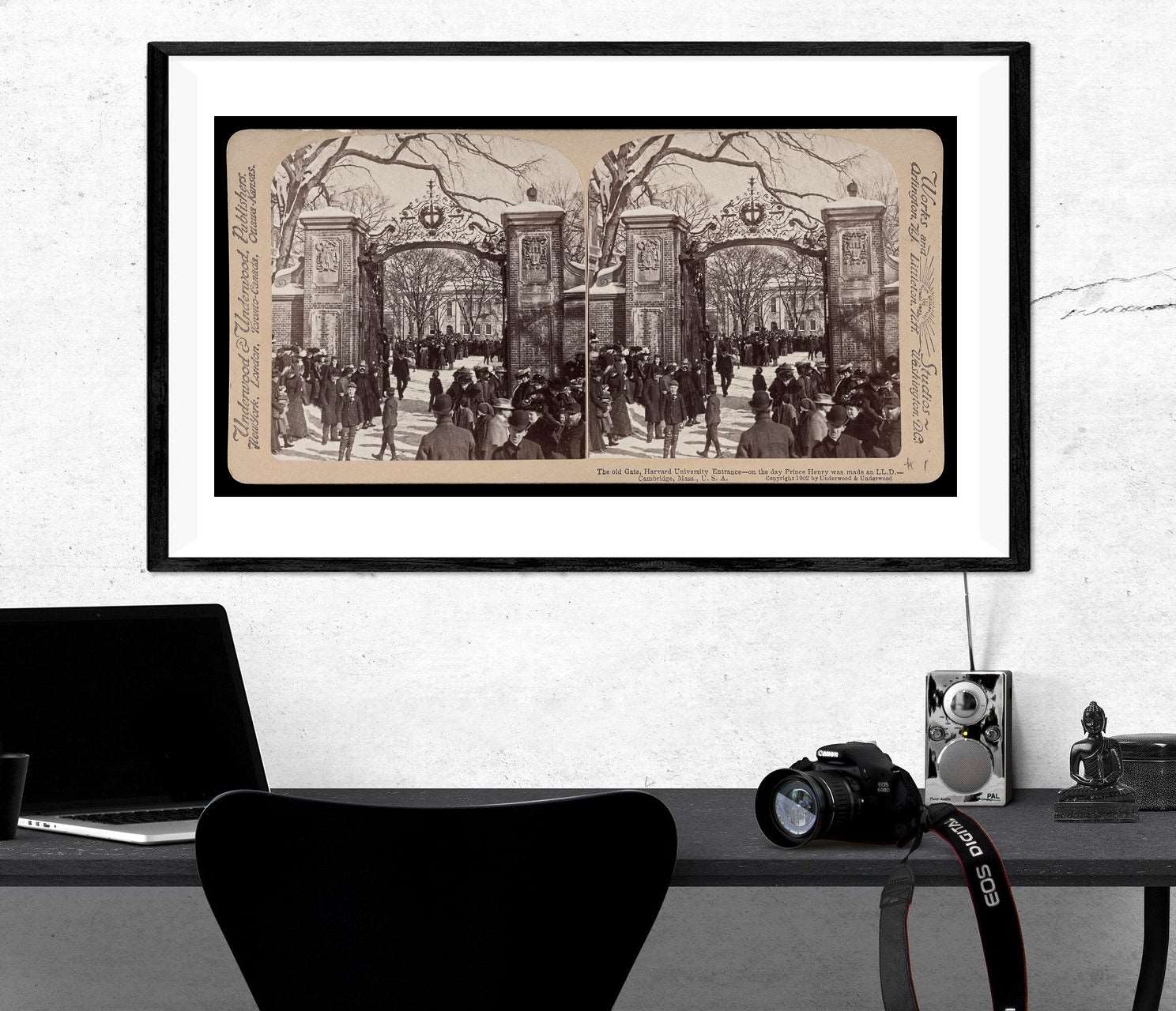 A framed print of a vintage stereograph image hanging above a black desk