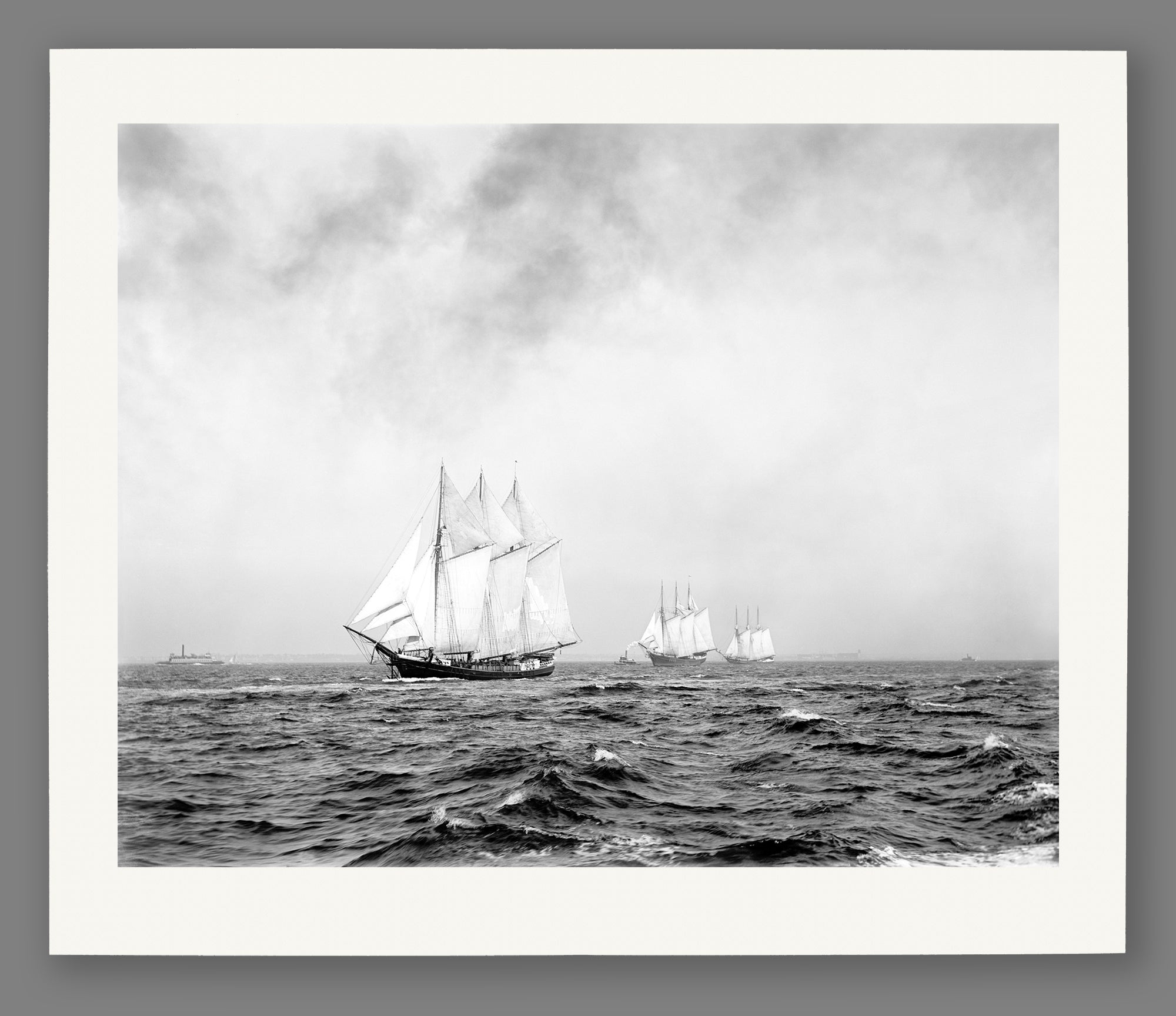 A paper print reproduction of a photograph of a group of three-masted ships on the ocean