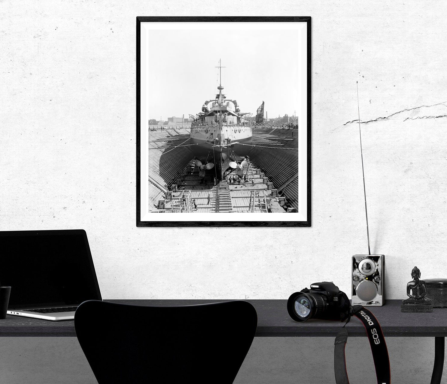 A framed paper print of a ship in Brooklyn Navy Yard's dry dock hanging on a rustic wall above a desk