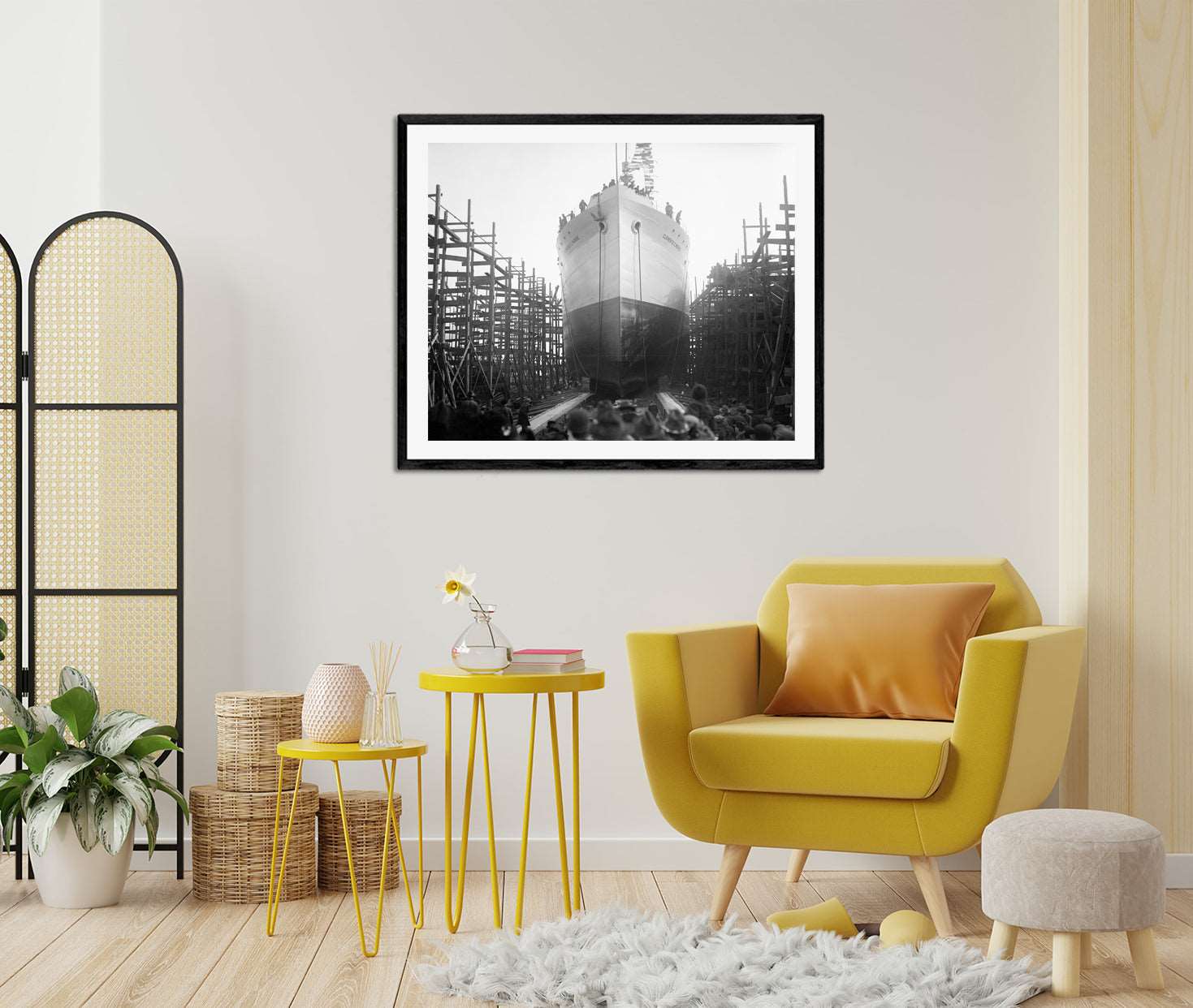 A room with yellow furniture and a framed paper print of a vintage photograph of a ship launch on the wall