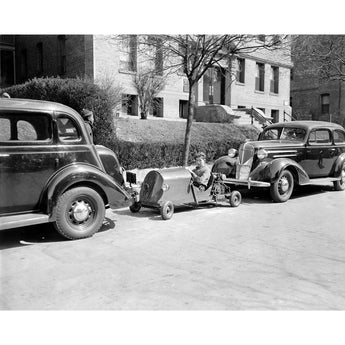A black and white, vintage photograph of a boy in Washington DC parking his miniature car on the street
