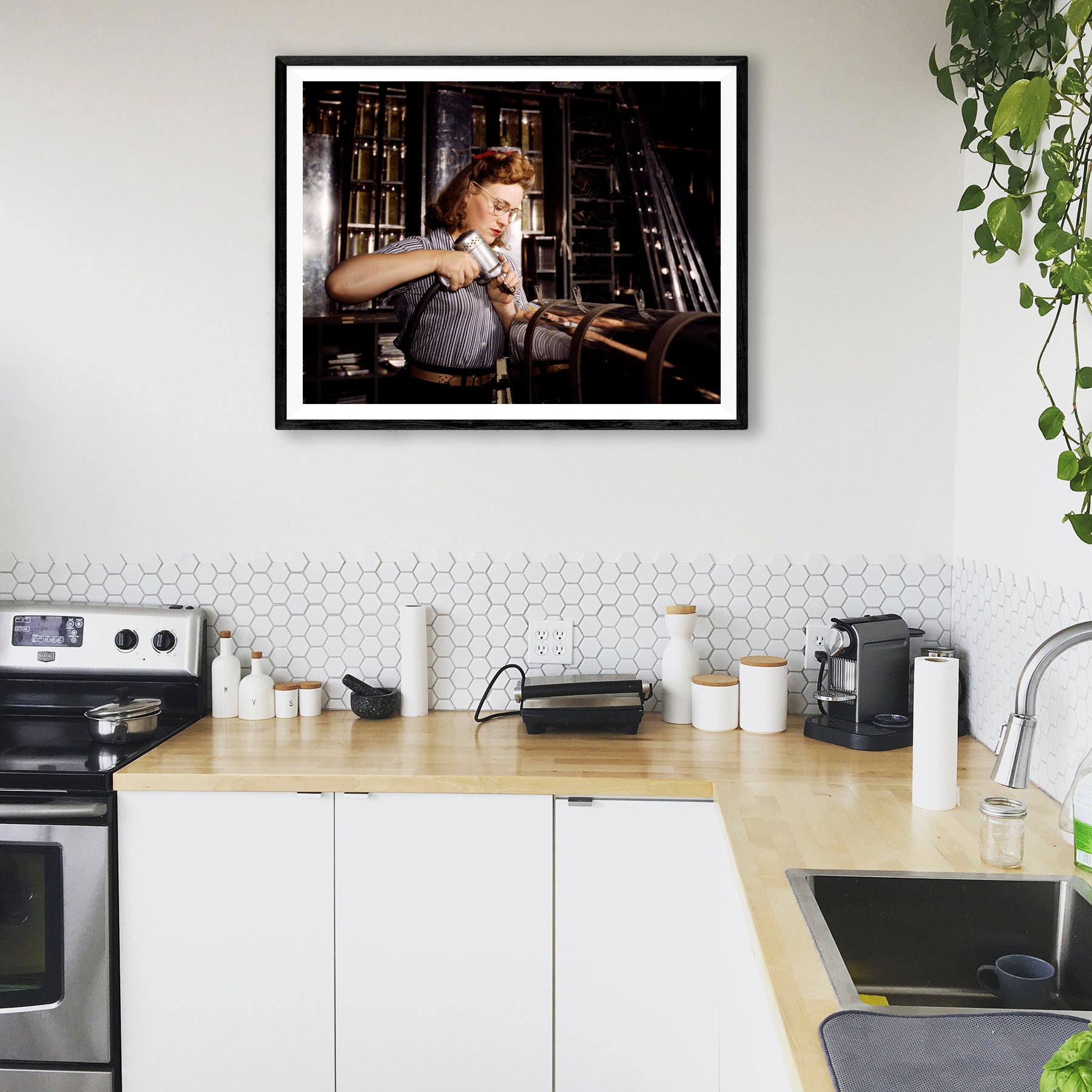 A mockup of a framed paper print hanging in a kitchen, featuring a vintage photograph of a woman working at North American Aviation