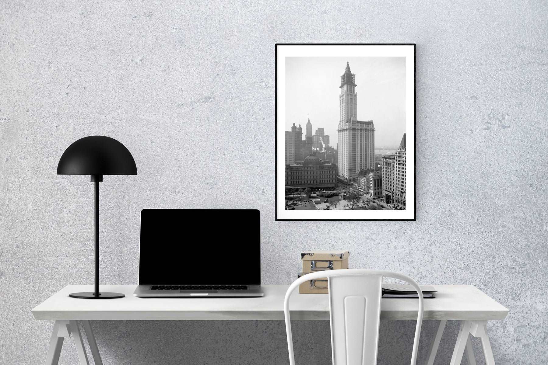 A framed print of the Woolworth Building in New York City, printed on paper and hanging above a desk