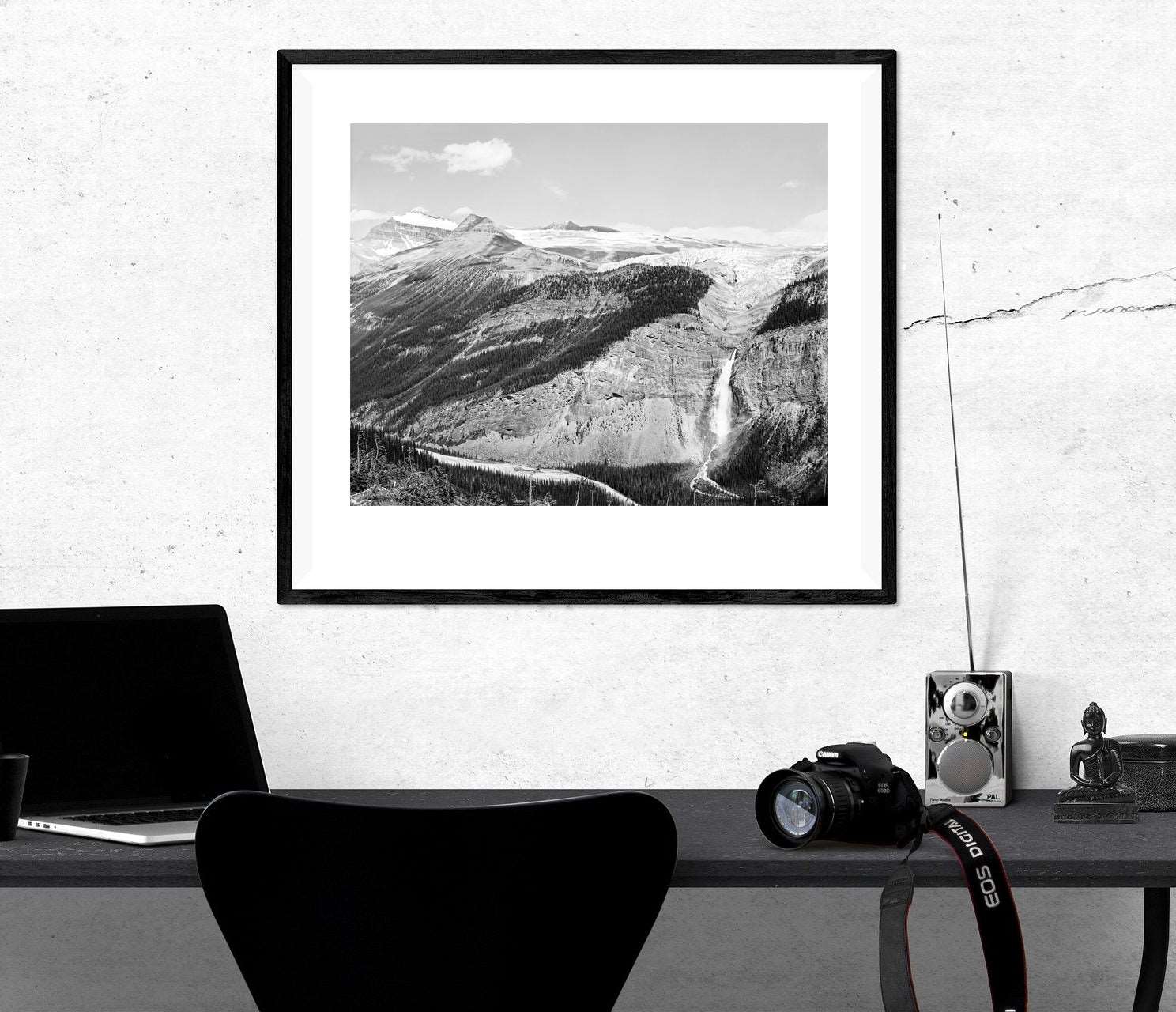A mockup of a framed paper print of a black and white photograph hanging above a work desk